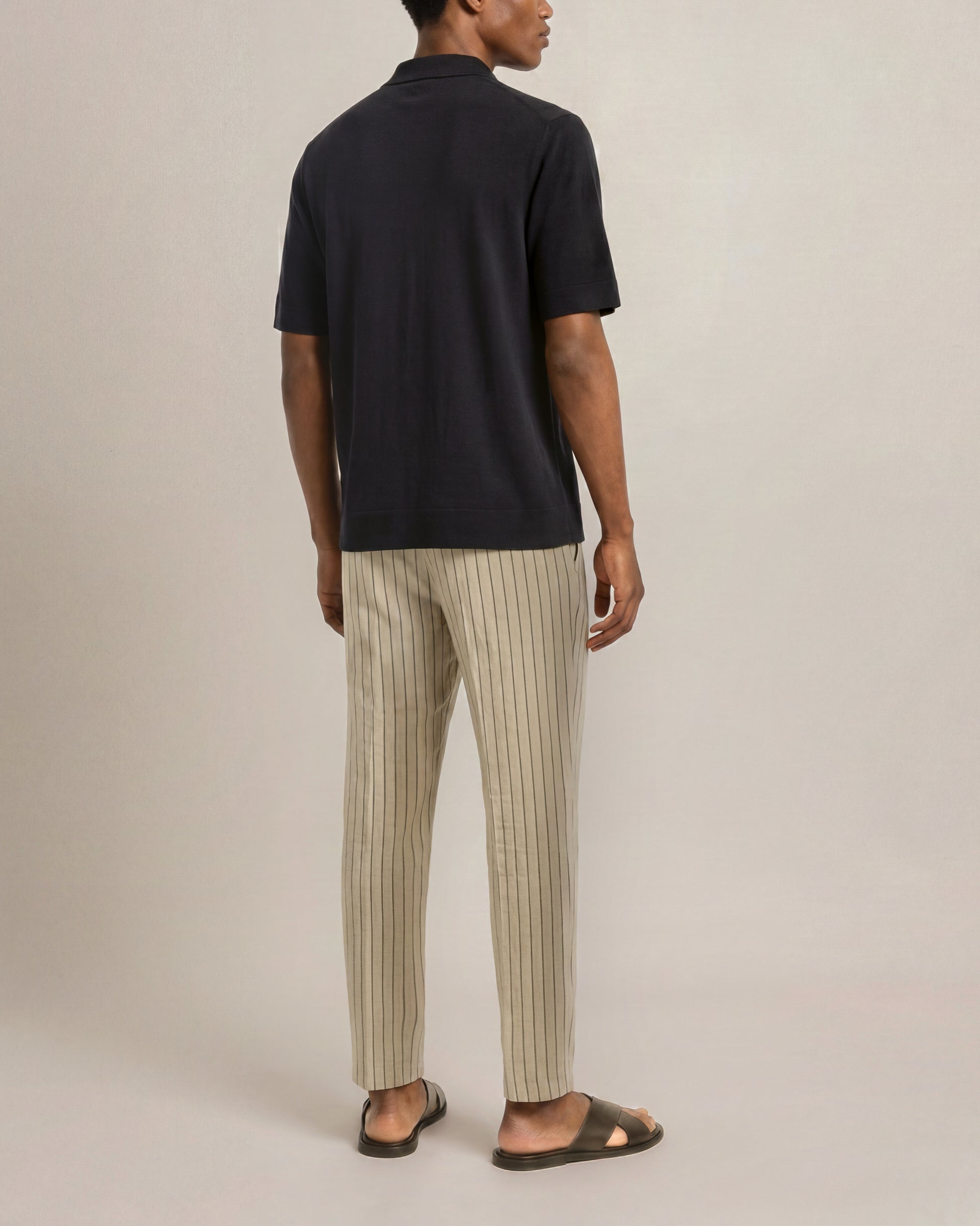 Person wearing a black polo shirt and beige striped pants on a plain background