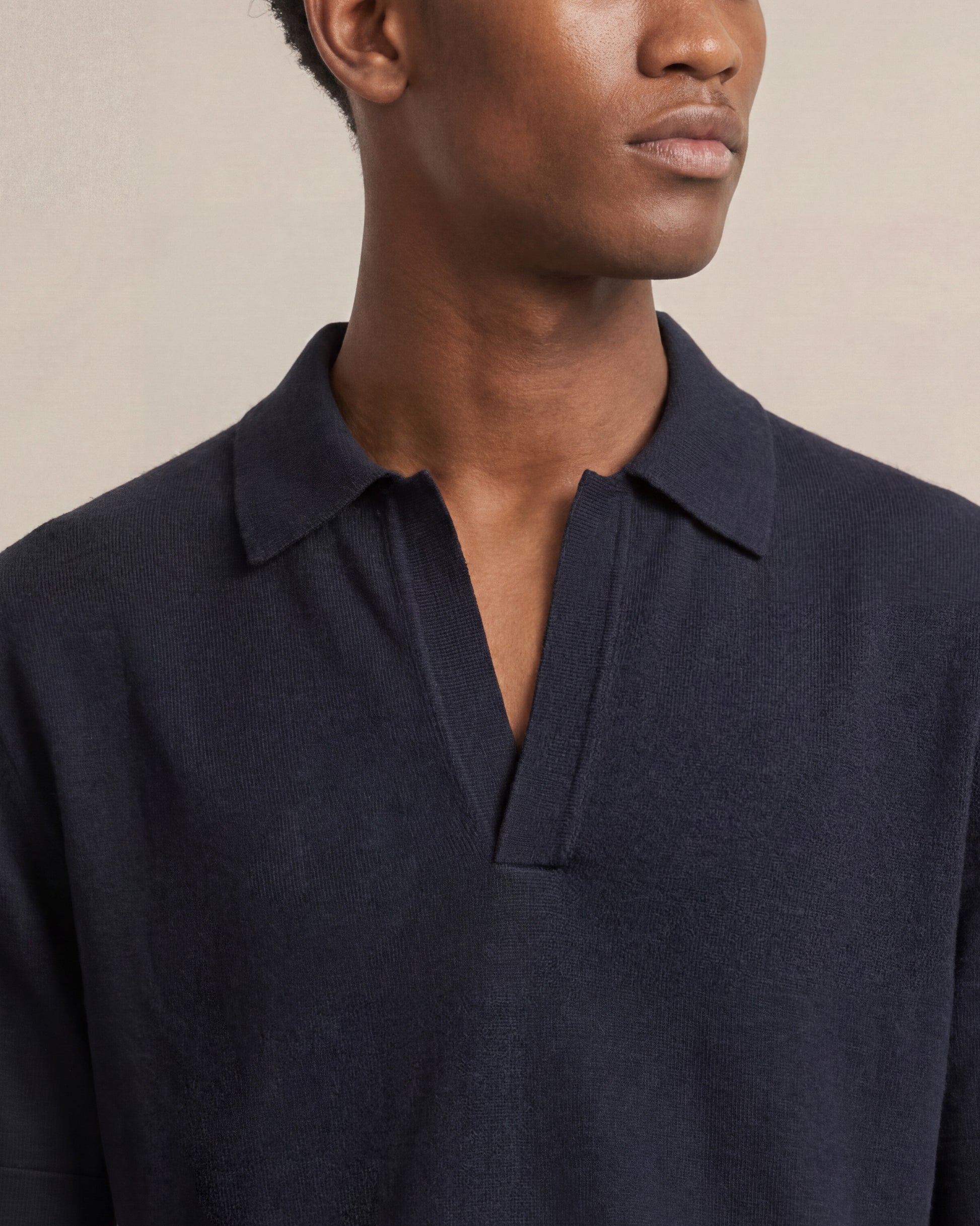 Man wearing a navy blue polo shirt against a beige background