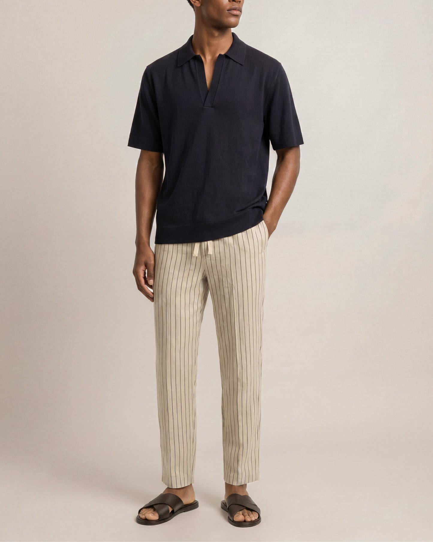 Man wearing a dark polo shirt and striped pants on a plain background
