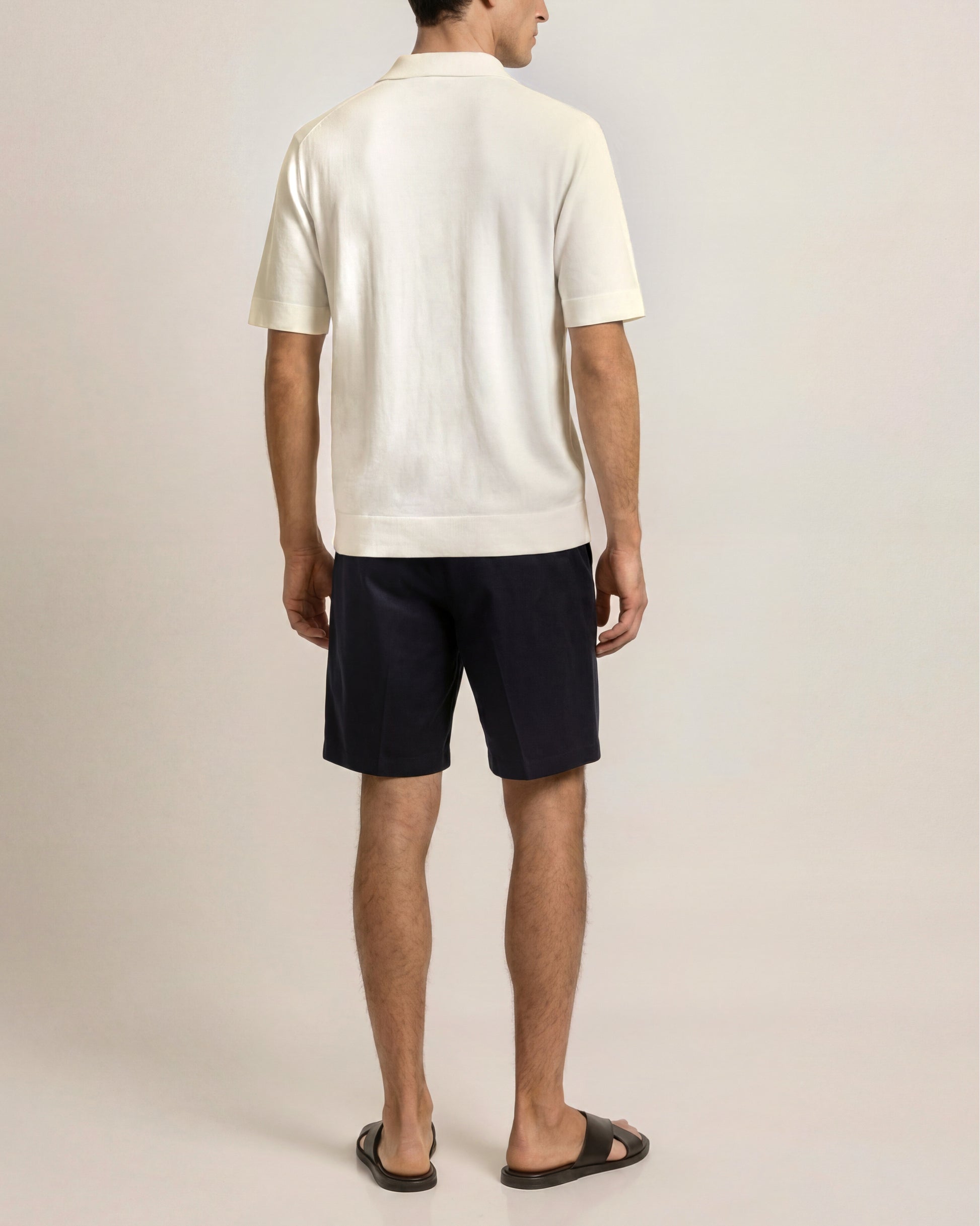Man wearing a white polo shirt and black shorts on a plain background