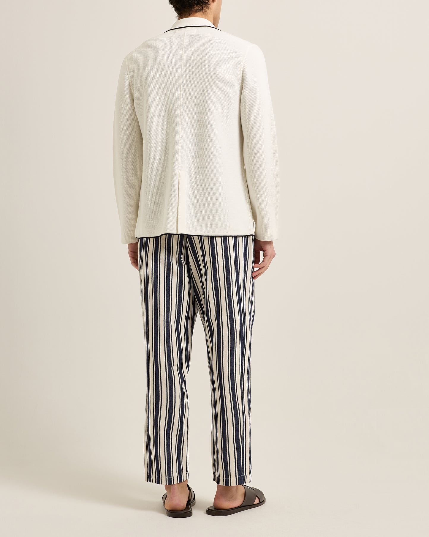 Person wearing a white blazer and striped pants on a plain background