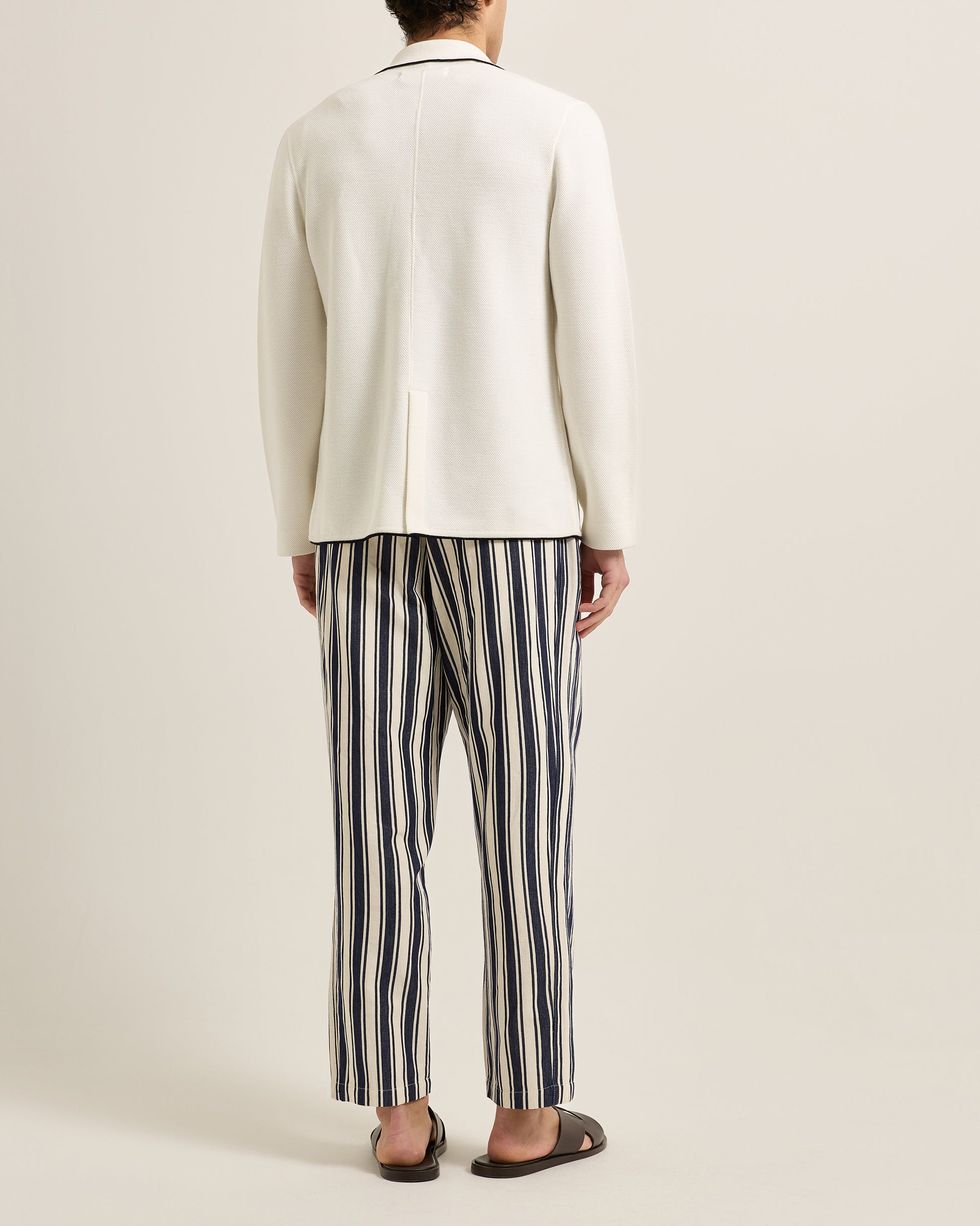 Person wearing a white blazer and striped pants on a plain background