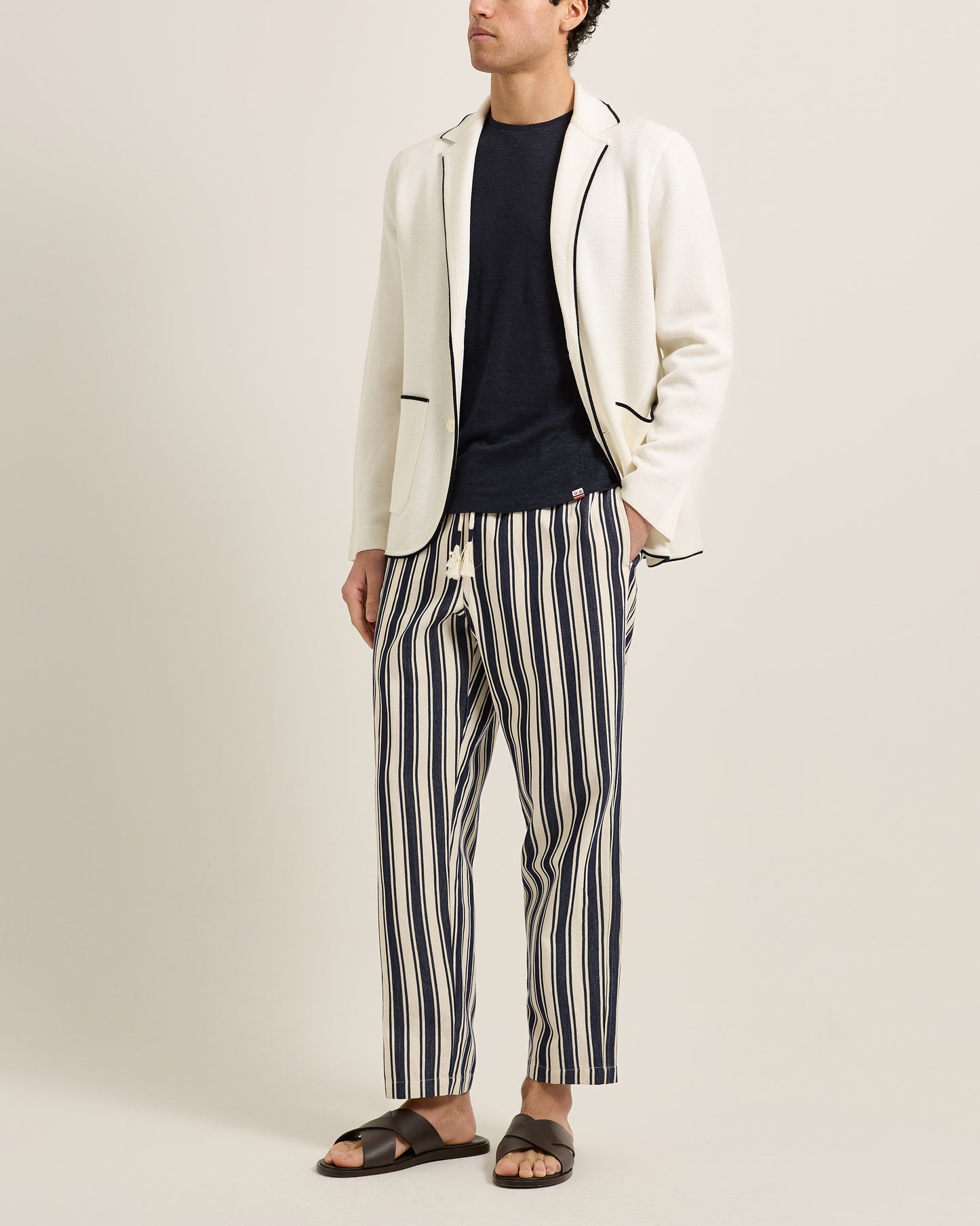 Person wearing a white blazer, black t-shirt, and striped pants on a plain background