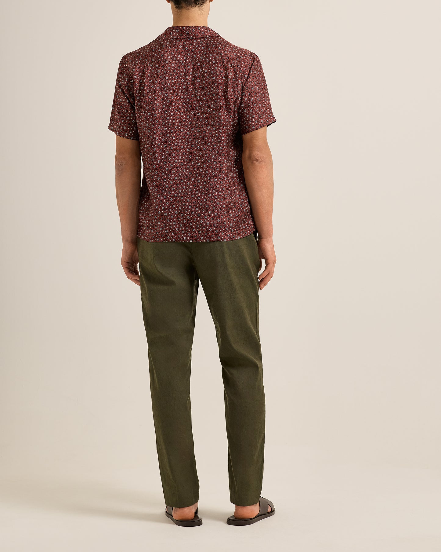 Person wearing a patterned shirt and Ray linen green pants on a beige background