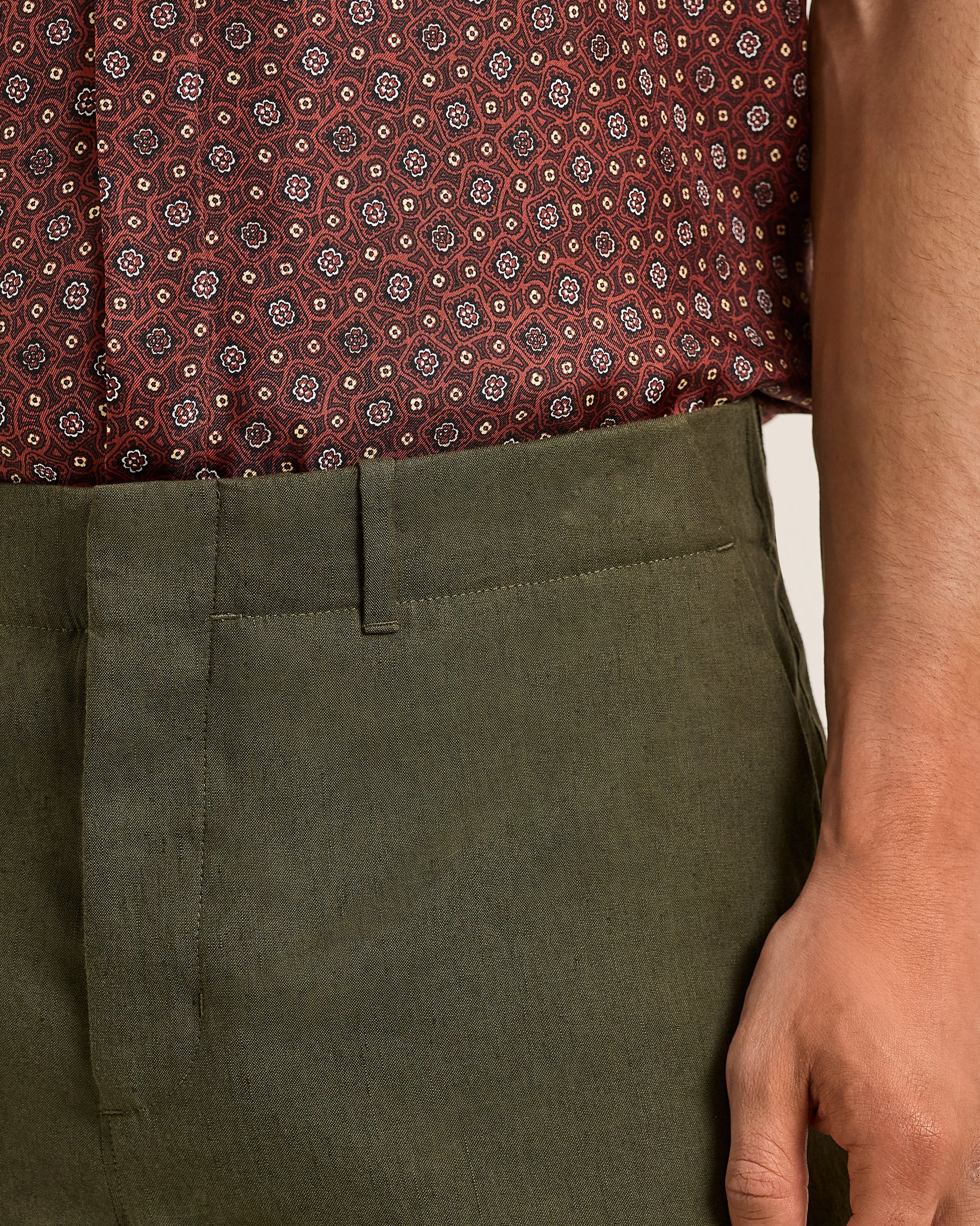 Close-up of a person wearing a patterned shirt and Ray linen green pants.