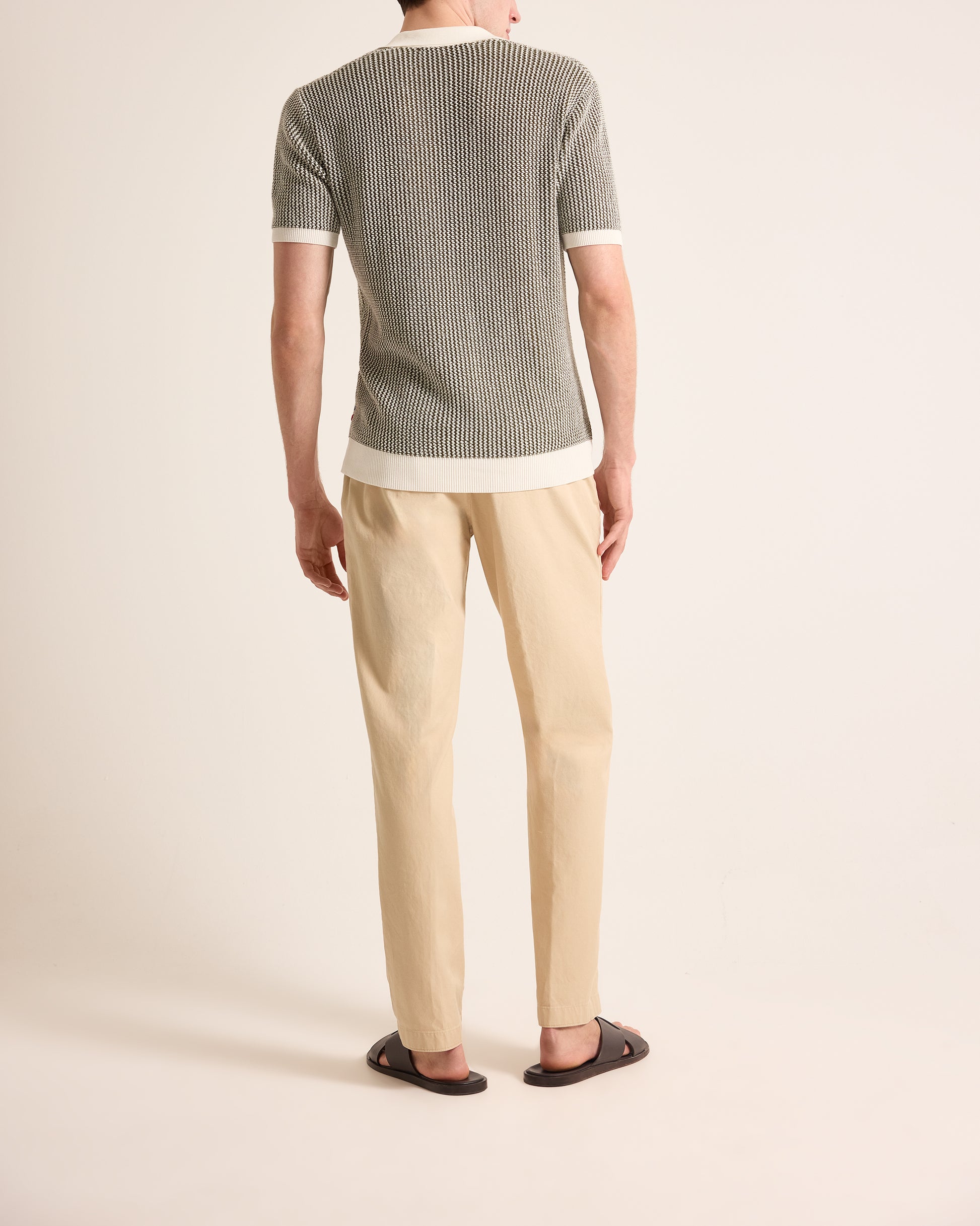 Person wearing a green and white striped shirt with beige pants on a plain background