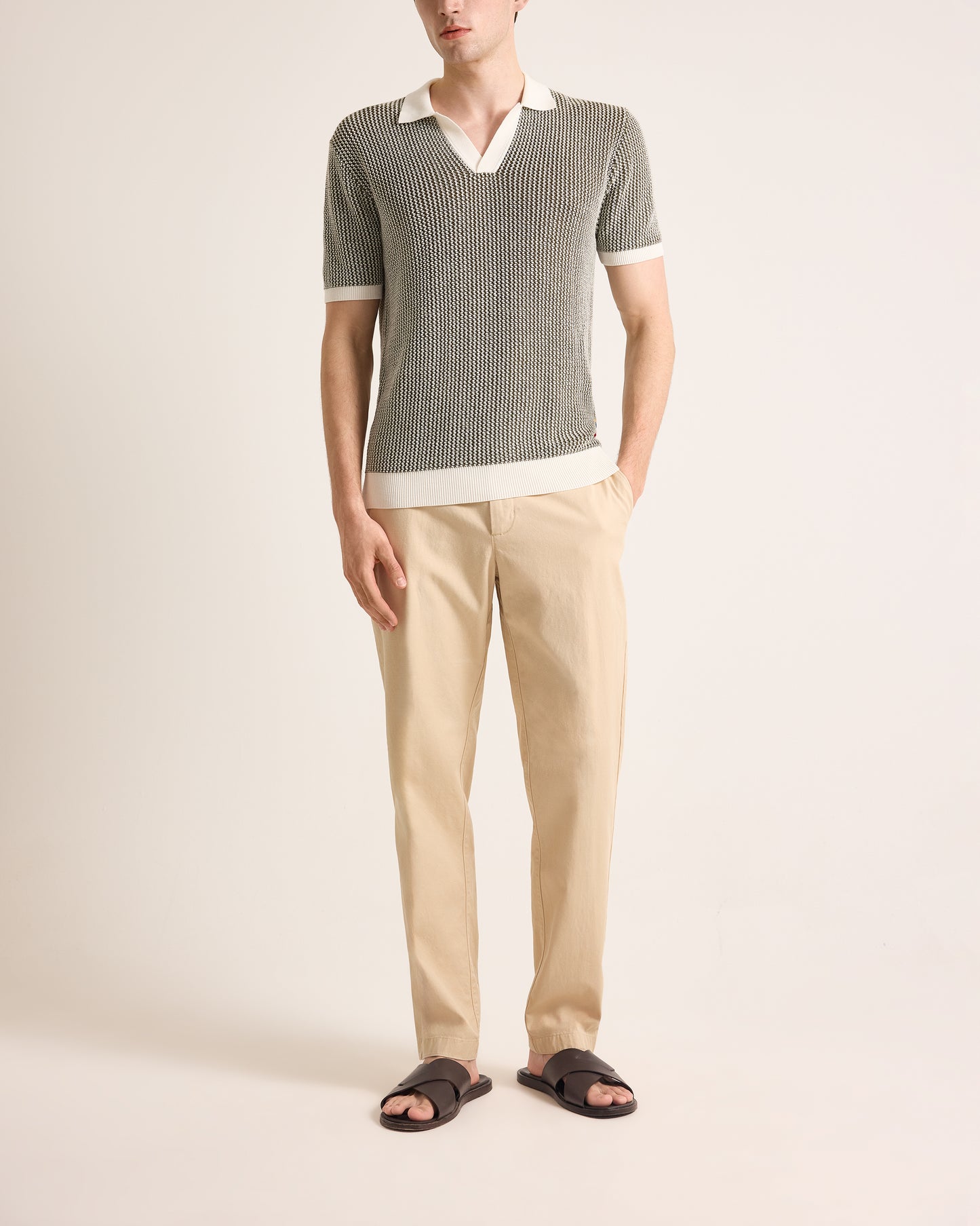 Man wearing a gray striped sweater with a white collar, beige pants, and sandals on a light background