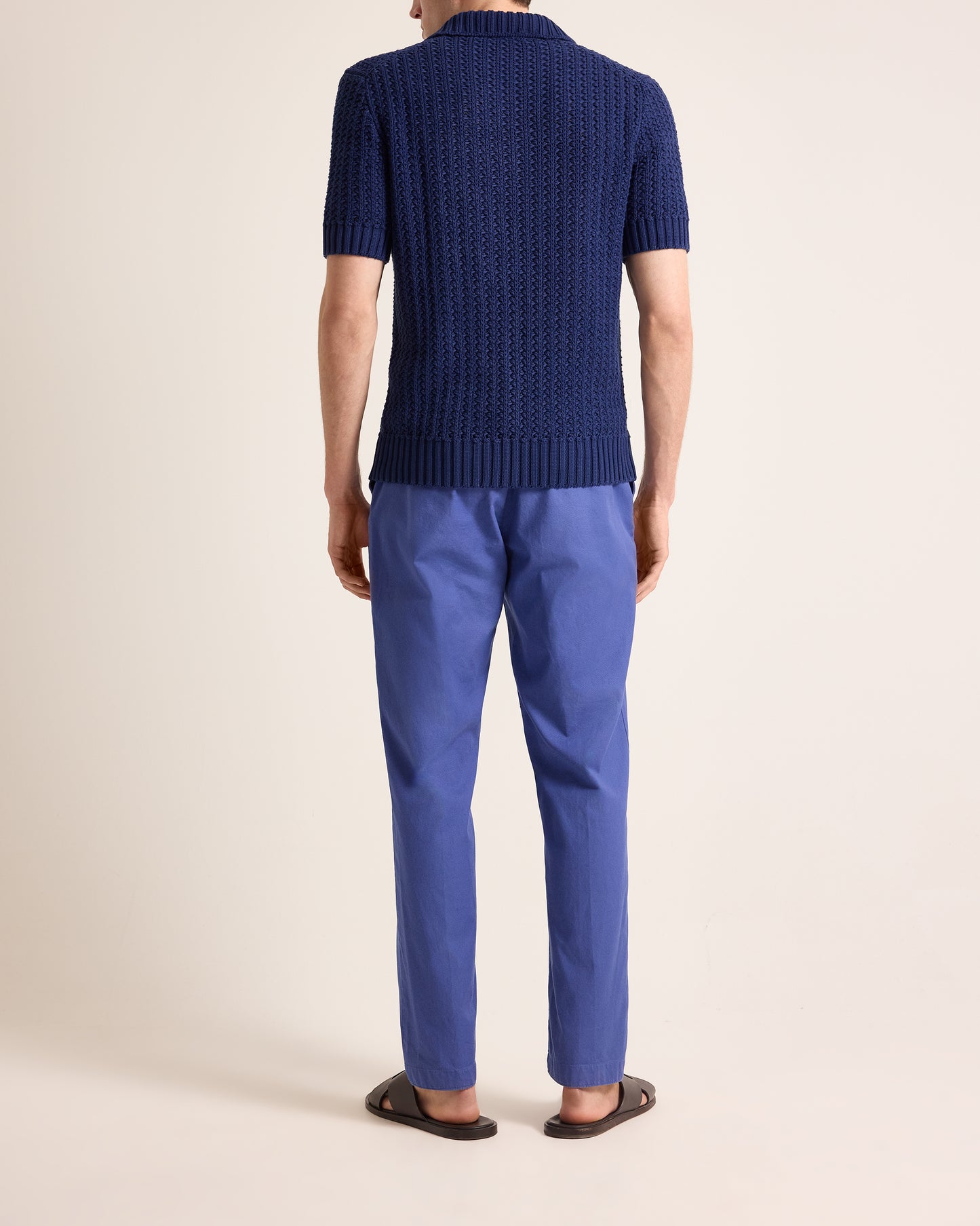 Person wearing a blue knitted sweater and matching pants on a beige background