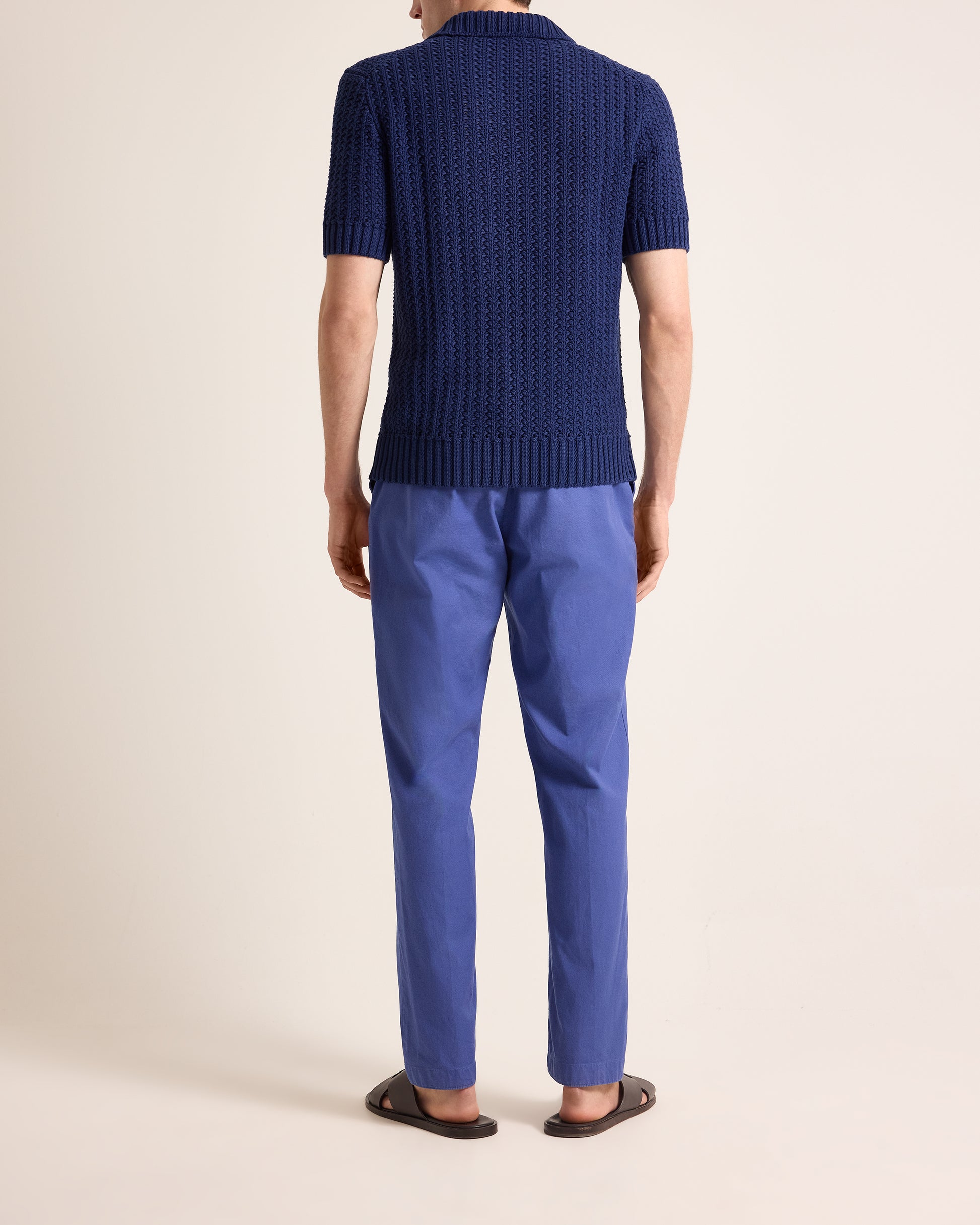 Person wearing a blue knitted sweater and matching pants on a beige background