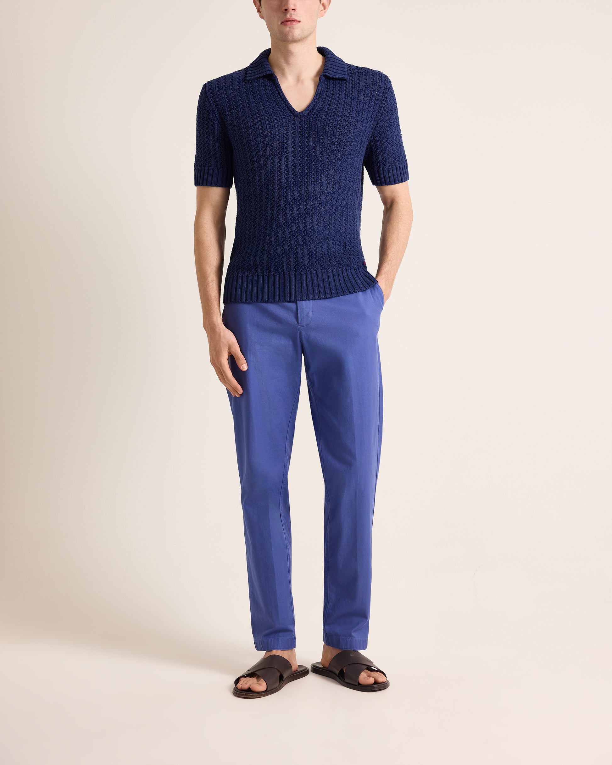 Person wearing a navy short-sleeve knit shirt and blue pants on a beige background