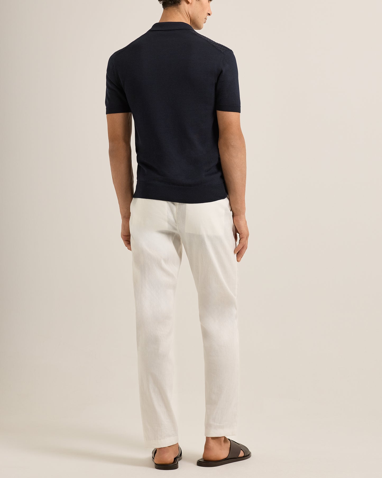 Person wearing a navy polo shirt and Ray linen tailored white trousers on a white background