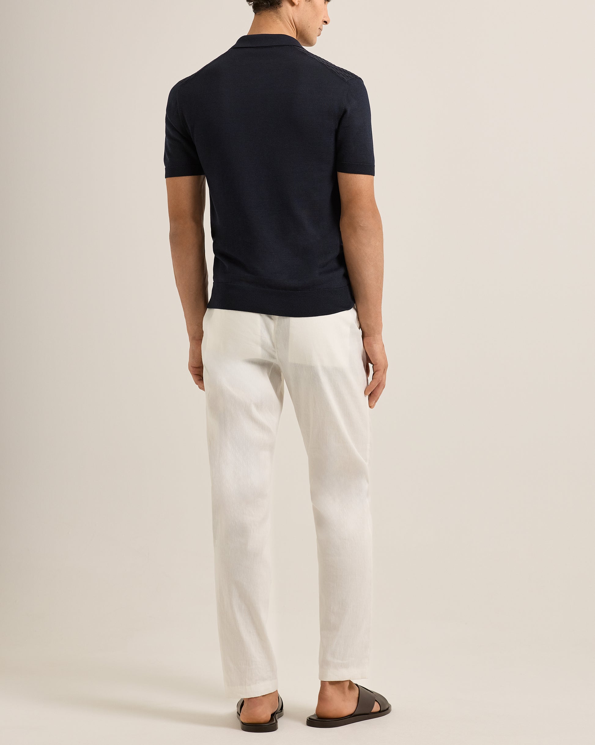 Person wearing a navy polo shirt and Ray linen tailored white trousers on a white background