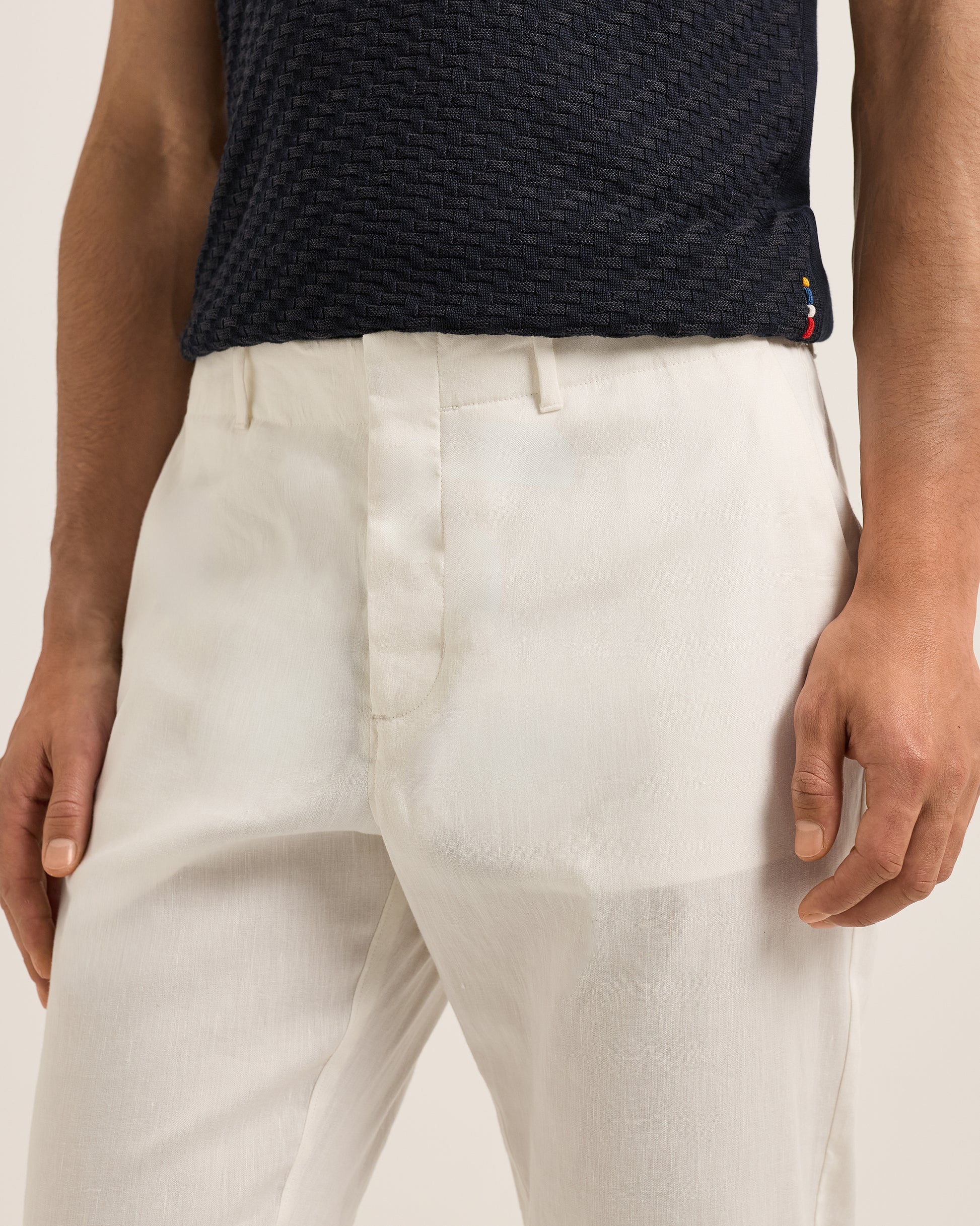 Person wearing a navy textured shirt and Ray linen tailored white trousers on a white background