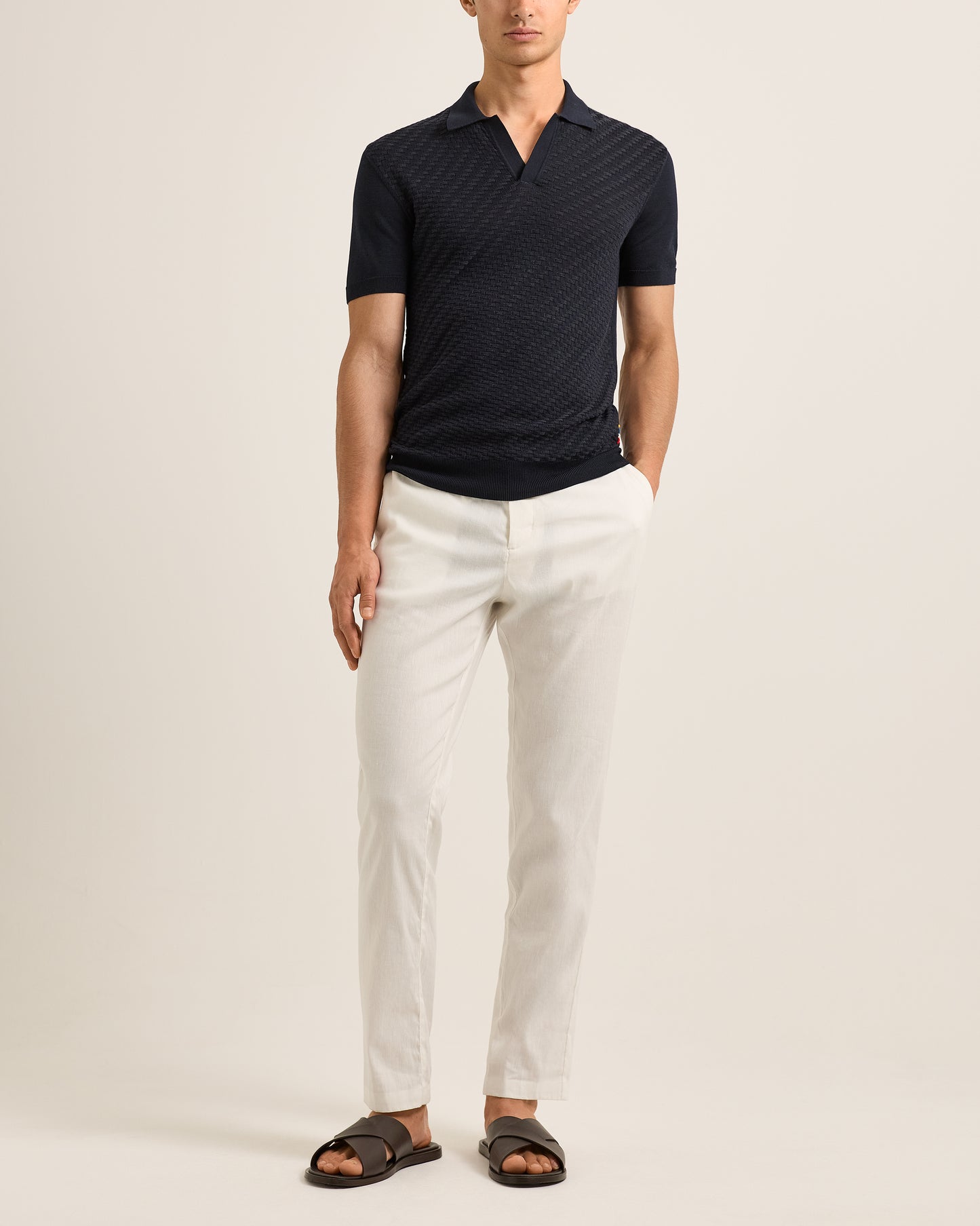 Man wearing a dark polo shirt and Ray linen tailored white trousers on a white background