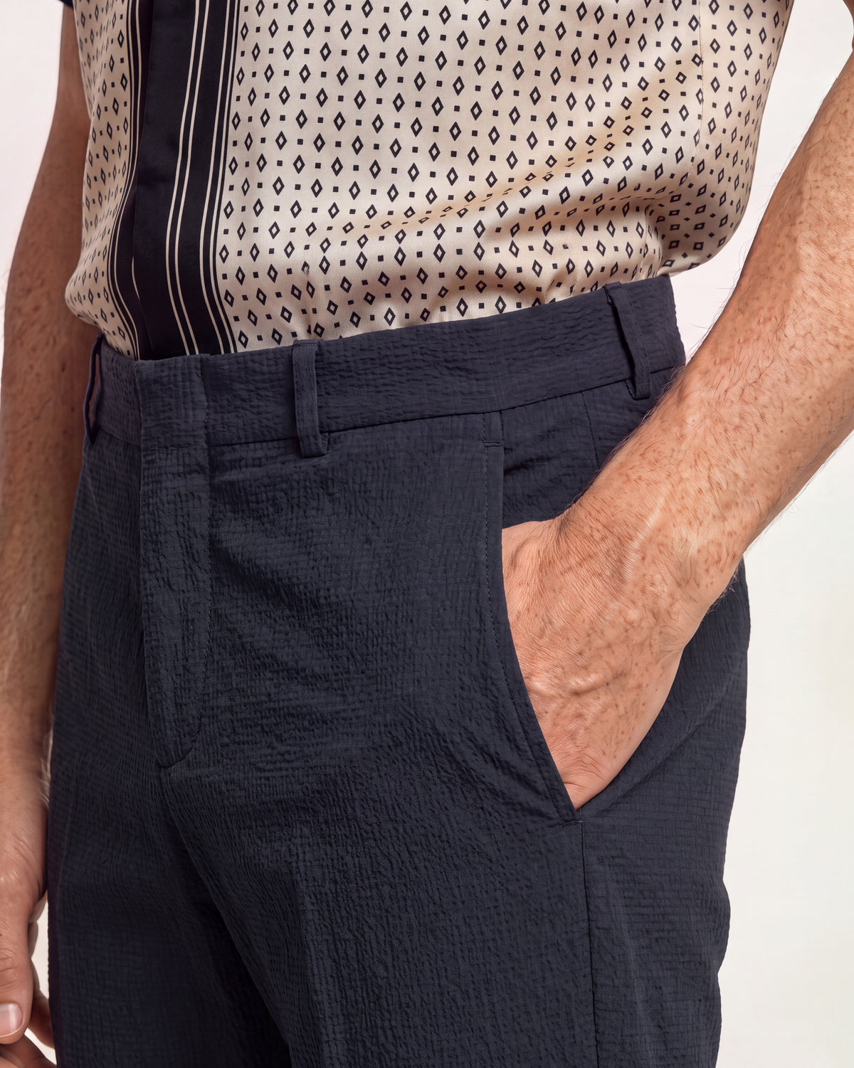 Closeup of navy tailored trousers and patterned silk shirt on a plain background