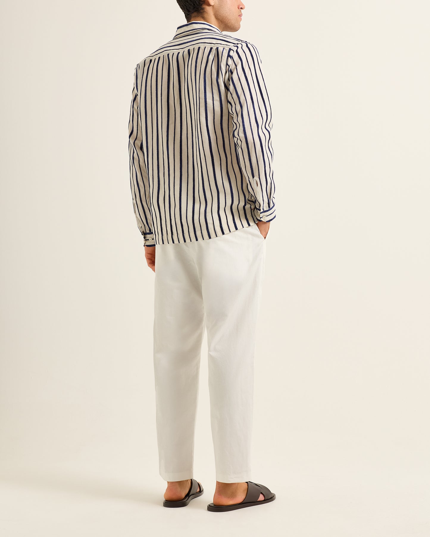 Person wearing a striped shirt and white pants on a plain background