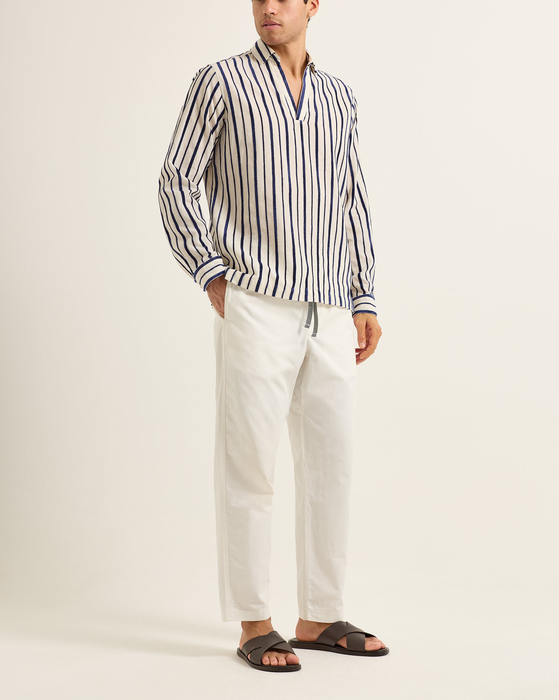 Man wearing a striped shirt and white pants on a plain background