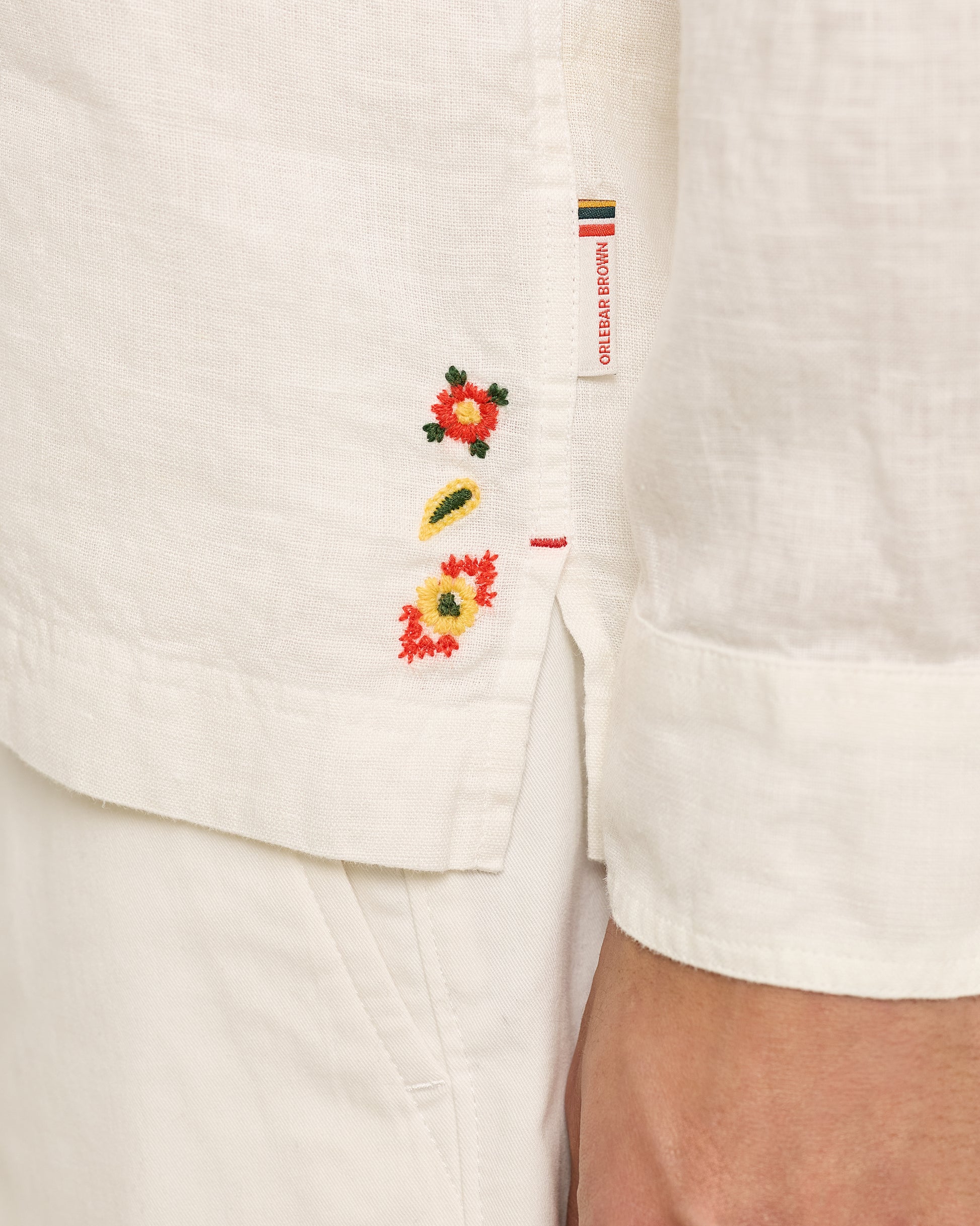 Close-up of a white garment with floral embroidery and a brand label.
