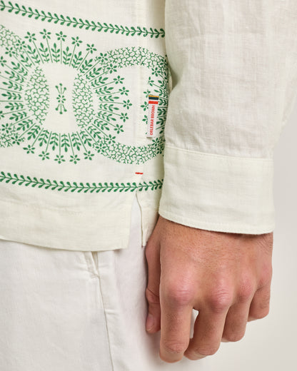 Close-up of a person wearing a white shirt with green embroidery on a plain background