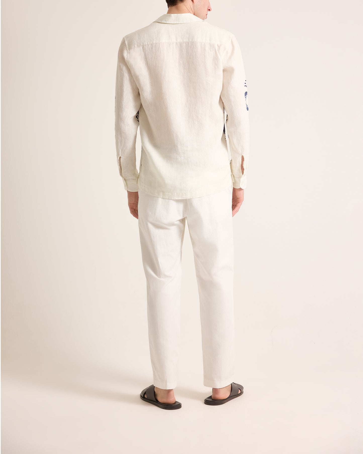 Person wearing a white linen shirt and pants on a plain background