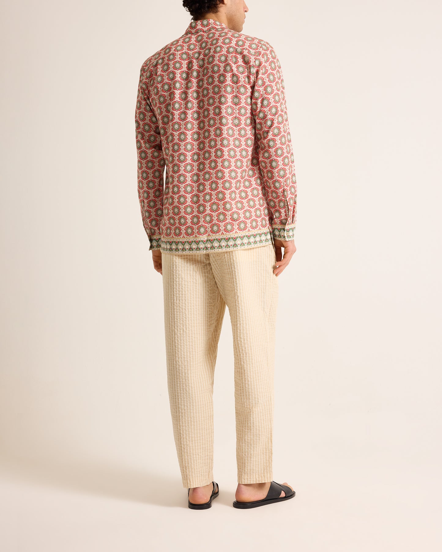 Person wearing a patterned shirt and beige pants on a white background