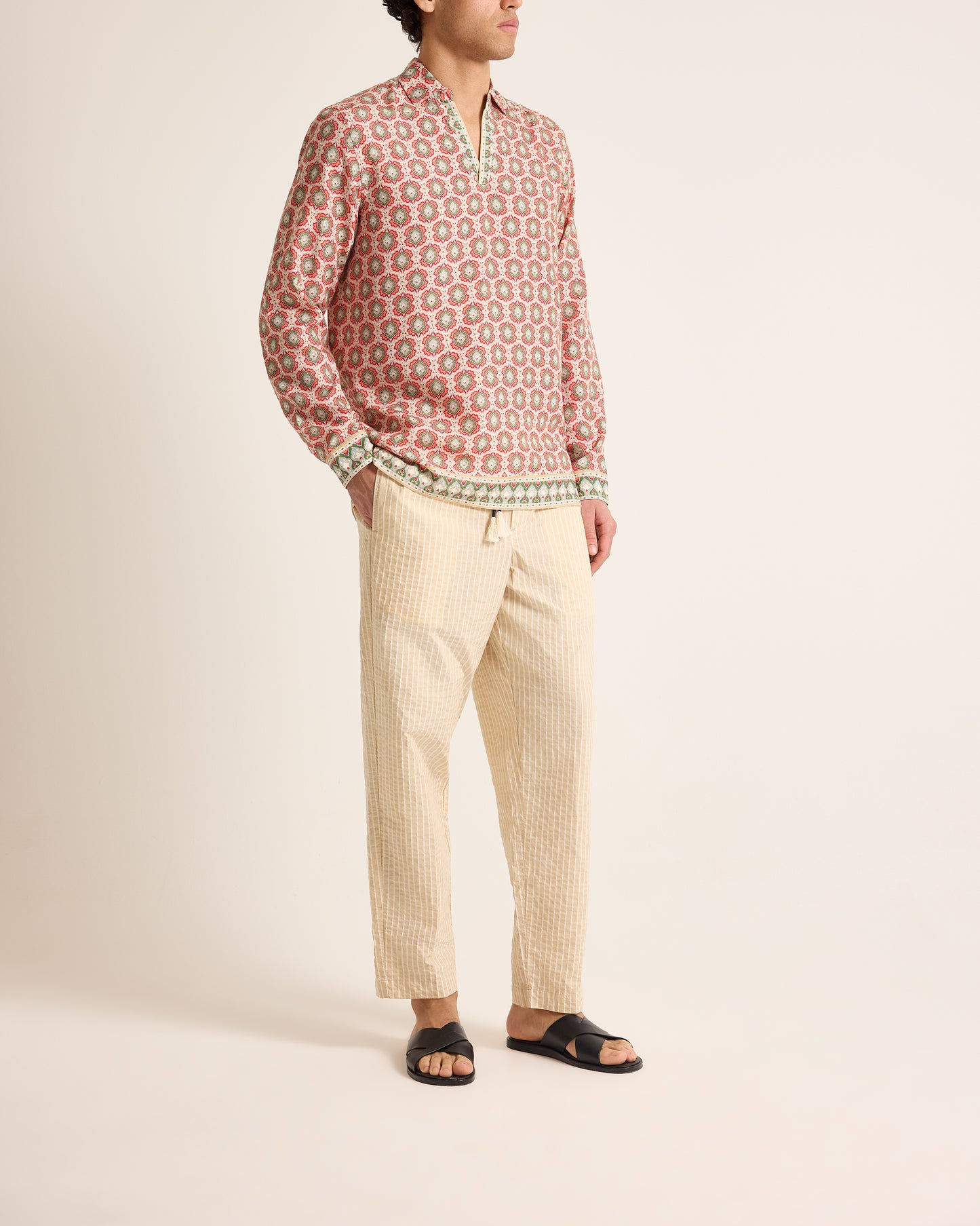 Person wearing a patterned shirt and beige pants on a plain background