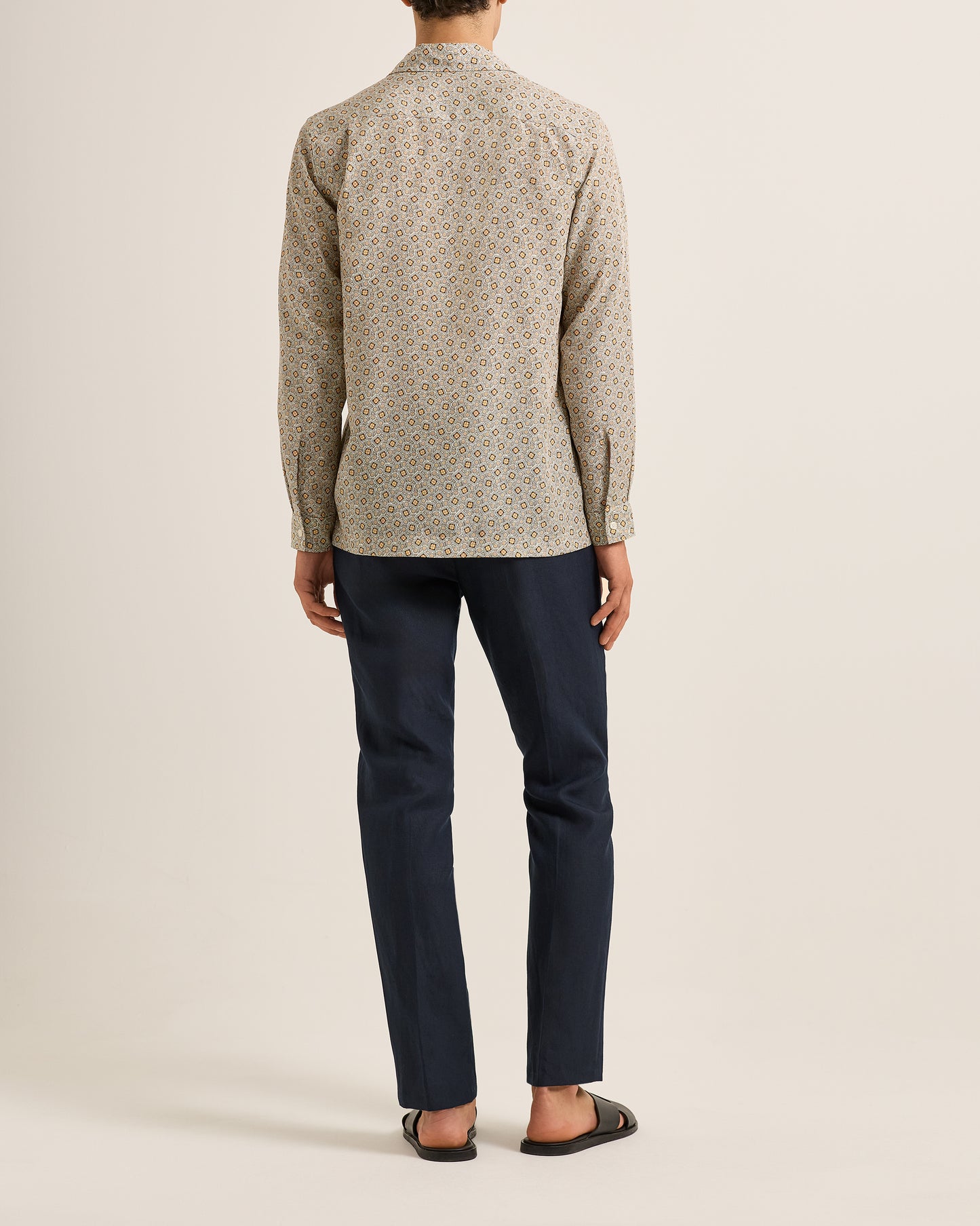 Person wearing a patterned shirt and dark pants on a plain background