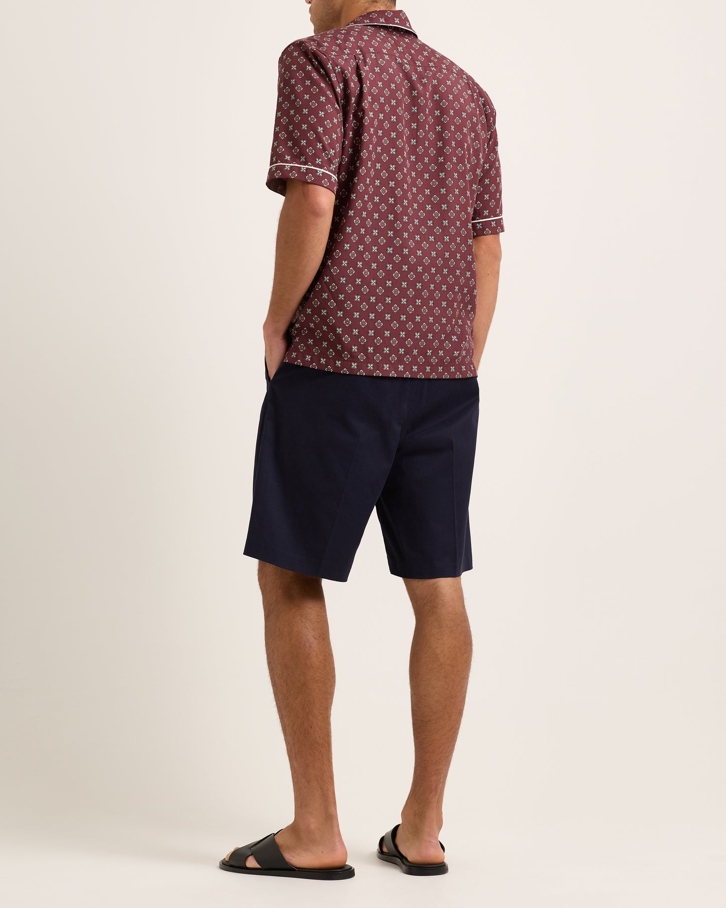 Model wearing maroon short-sleeved shirt with geometric pattern with navy shorts on white background