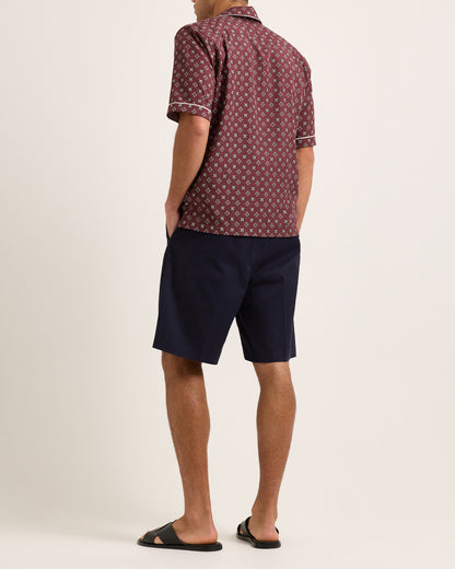 Model wearing maroon short-sleeved shirt with geometric pattern with navy shorts on white background