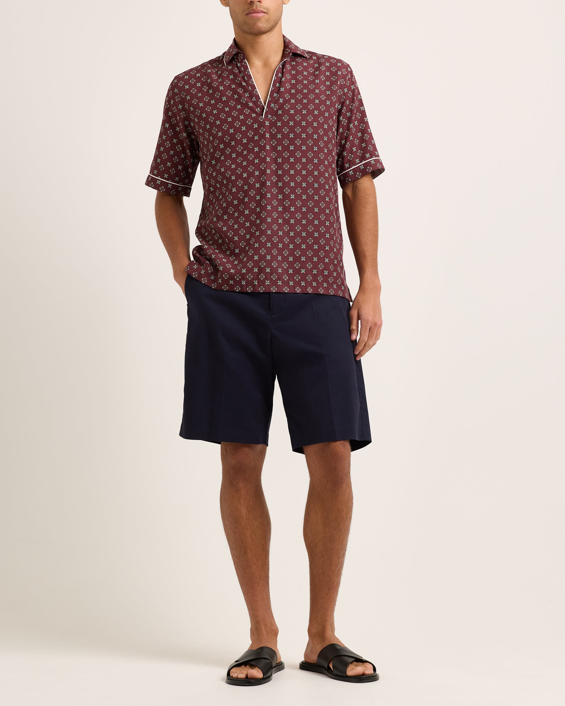 Model wearing maroon short-sleeved shirt with geometric pattern with navy shorts on white background
