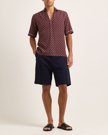 Model wearing maroon short-sleeved shirt with geometric pattern with navy shorts on white background