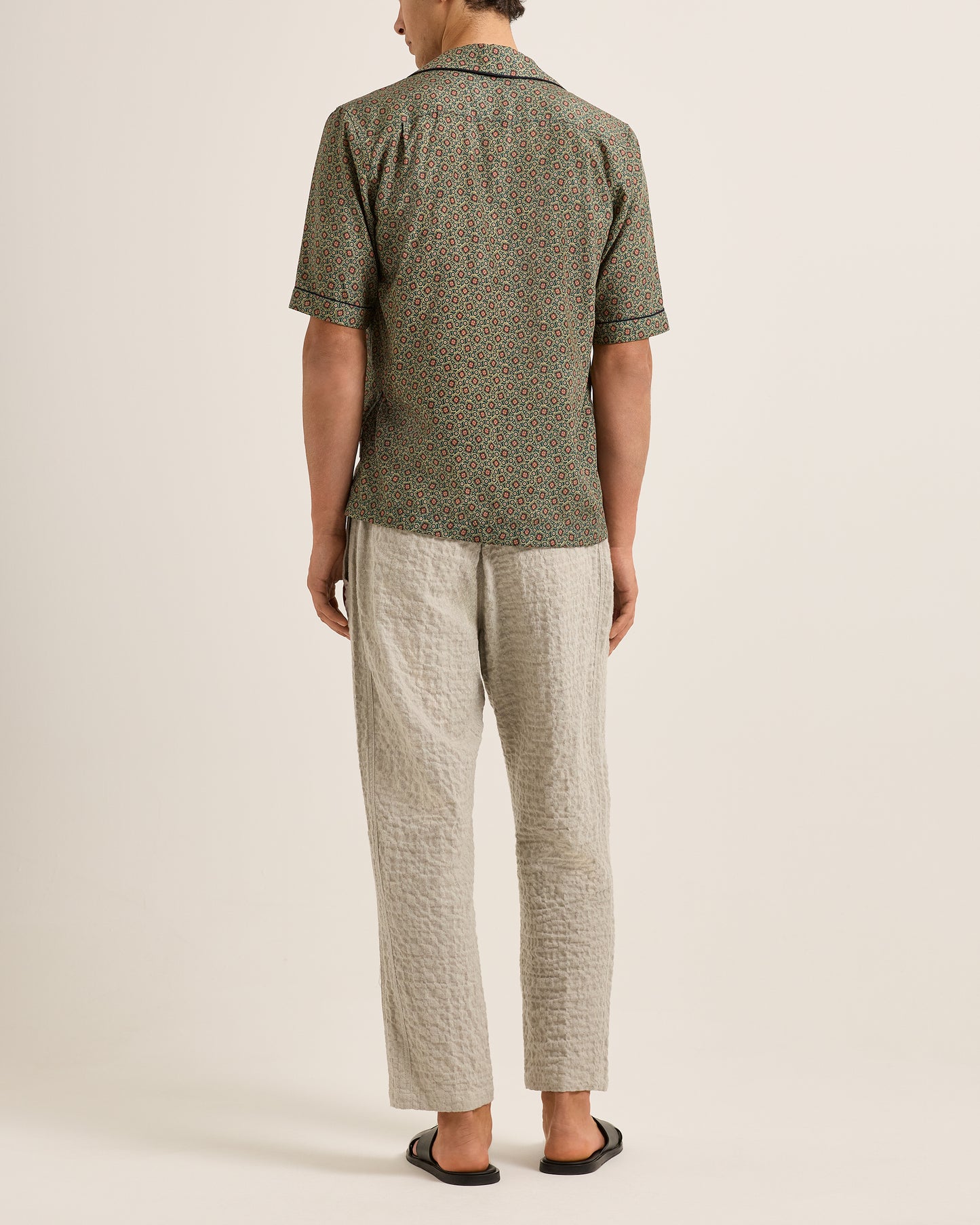 Person wearing a patterned shirt and light-colored pants on a plain background