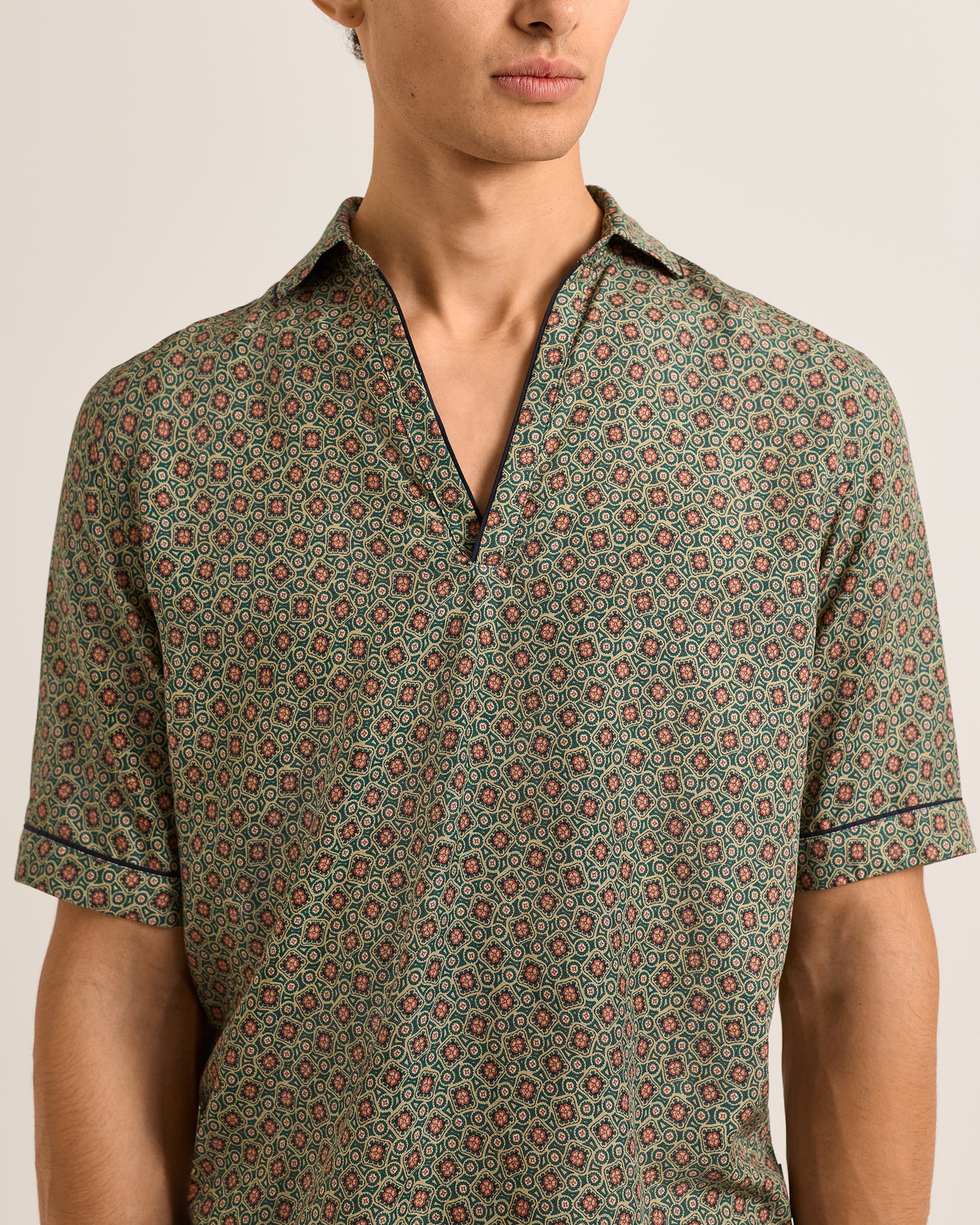 Man wearing a patterned green shirt against a neutral background