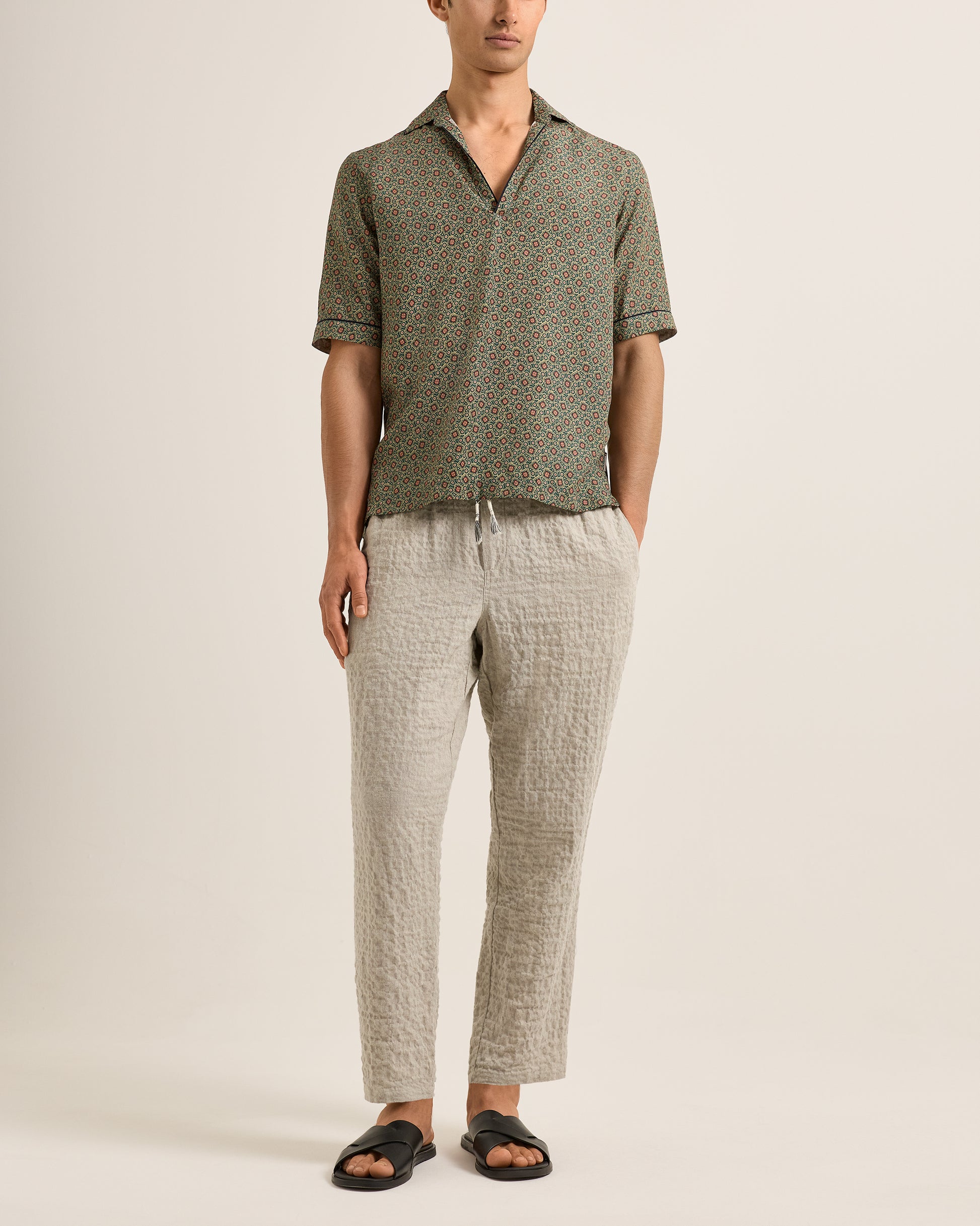 Person wearing a green patterned shirt and beige pants on a plain background
