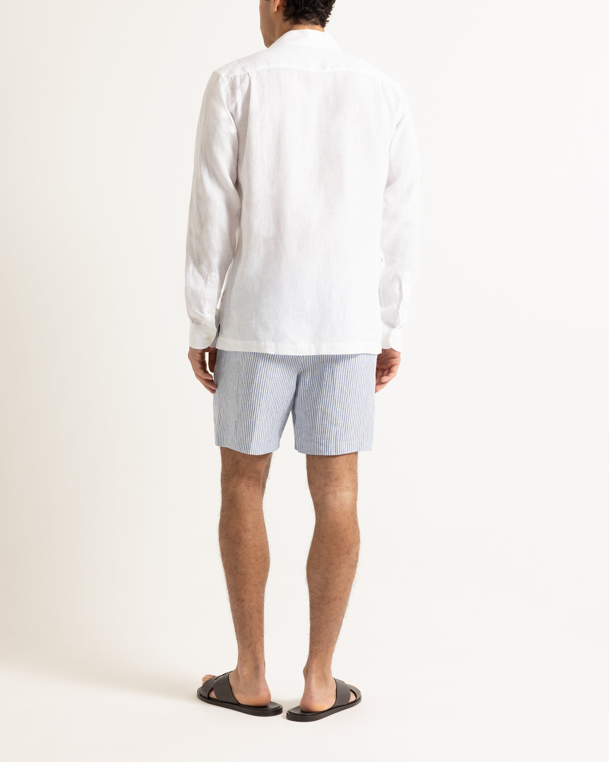 Man wearing white shirt with sun embroidery and blue and white striped shorts on a plain background