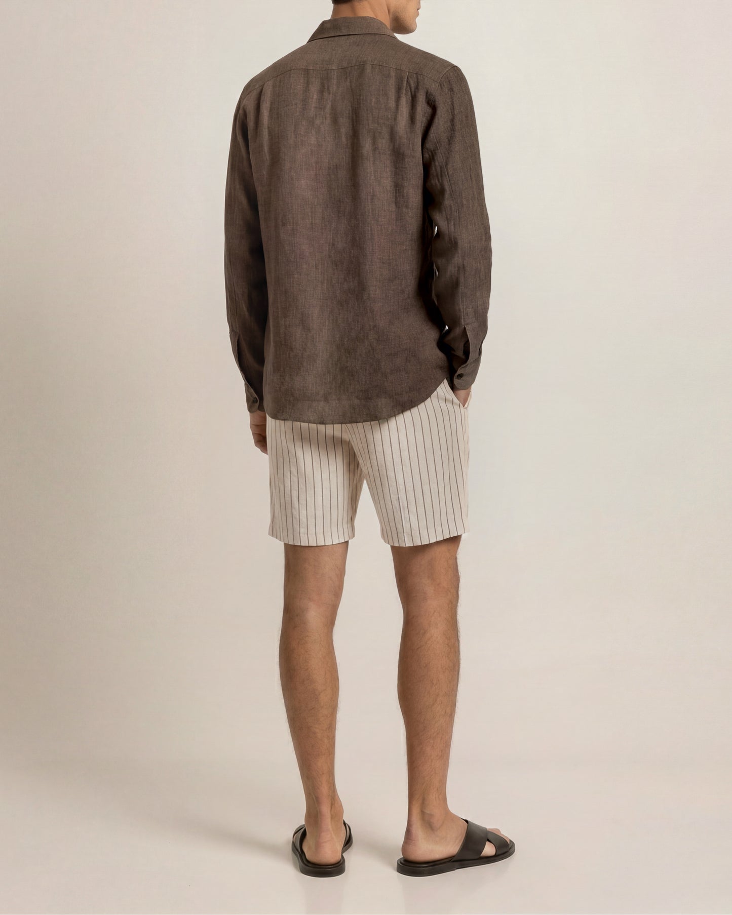Person wearing a brown jacket and beige shorts on a plain background