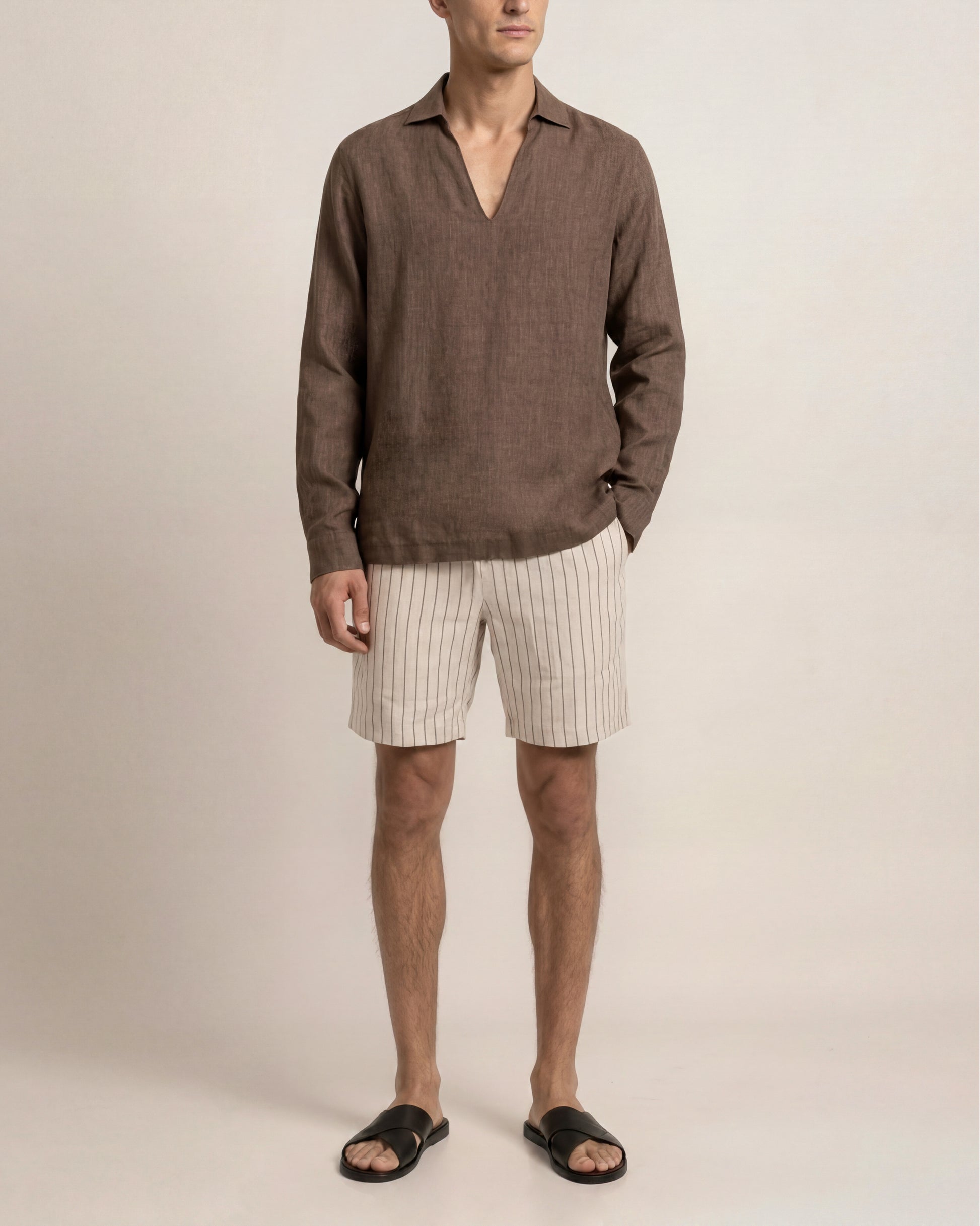 Man wearing a brown shirt and beige shorts against a plain background