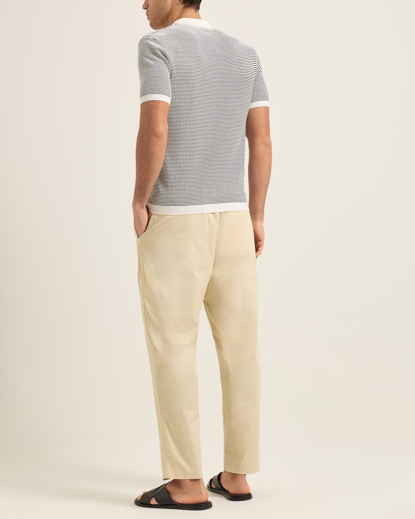 Person wearing a striped polo and beige pants on a plain background