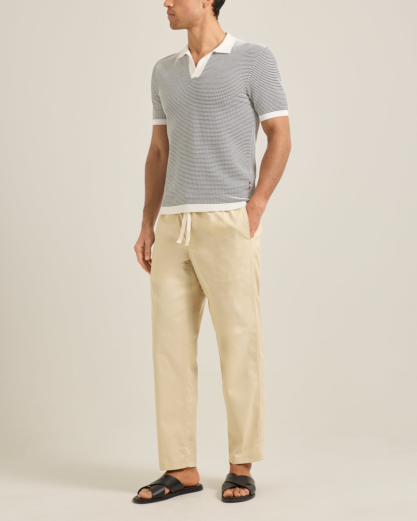 Man wearing a gray striped polo and beige pants on a plain background