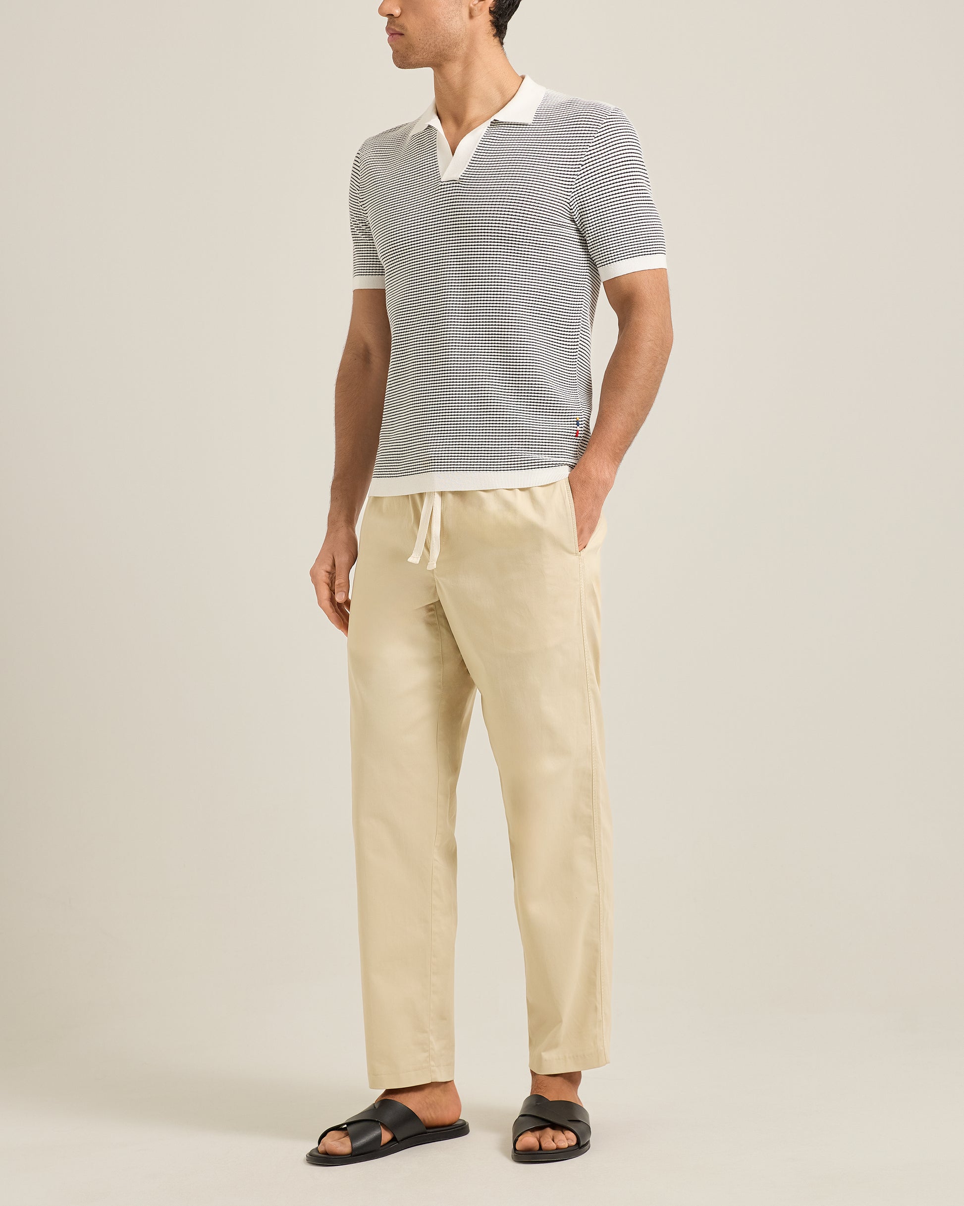 Man wearing a gray striped polo and beige pants on a plain background