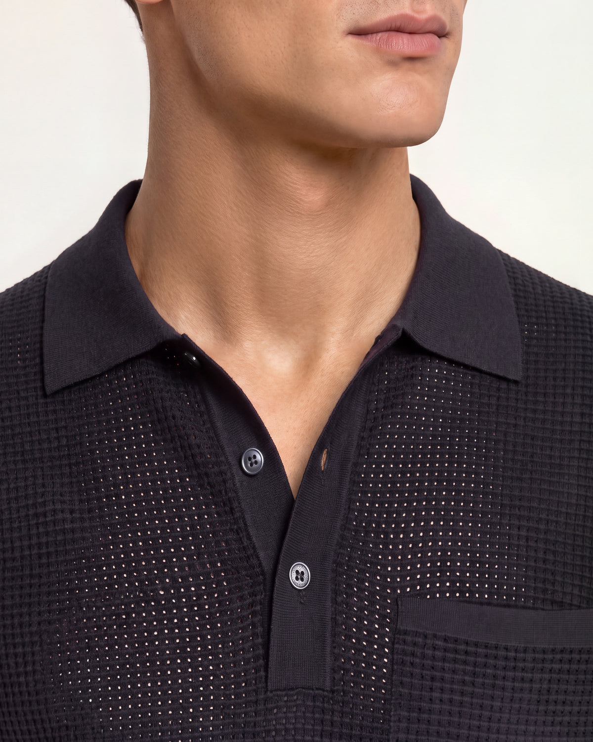 Closeup of navy mesh stitch polo shirt with pocket detail on a plain background