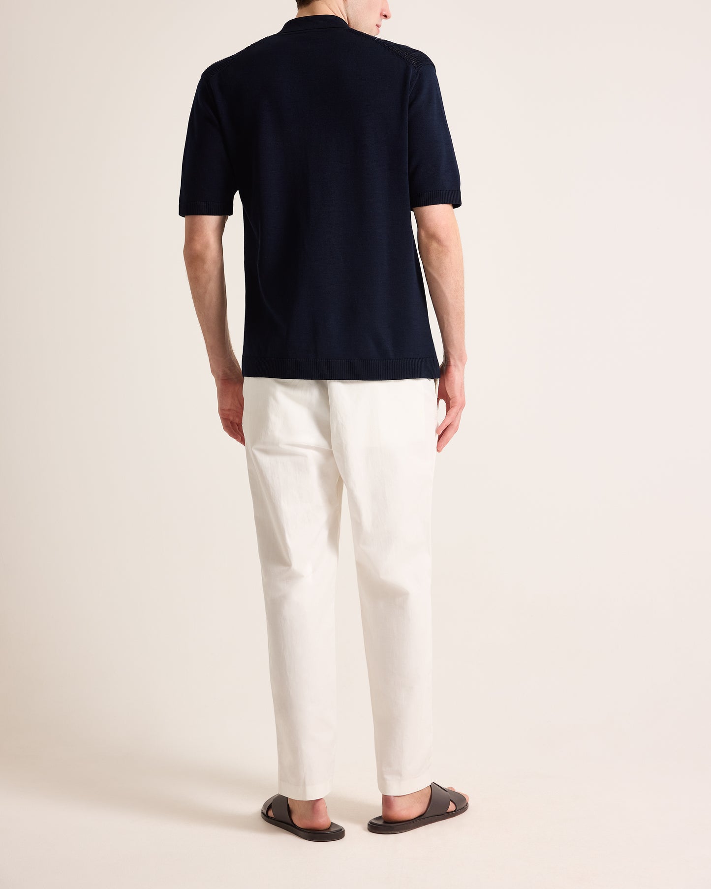 Person wearing a navy polo shirt and white pants on a plain background