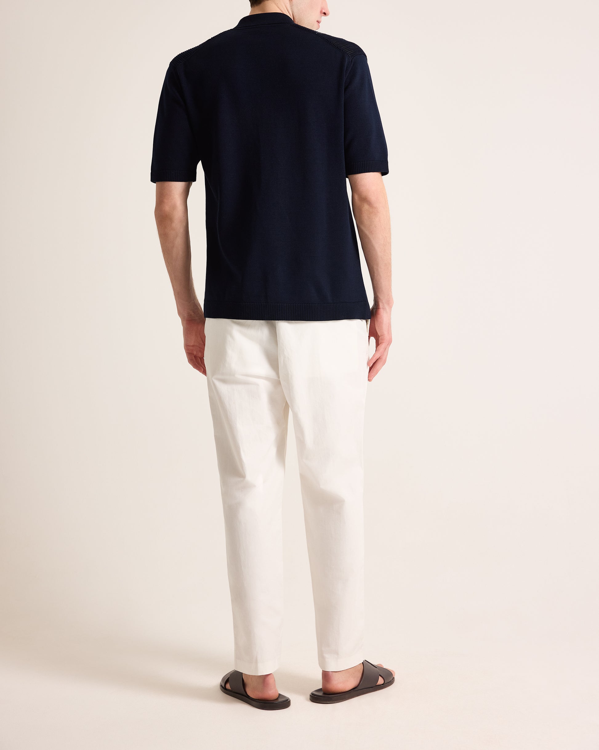 Person wearing a navy polo shirt and white pants on a plain background