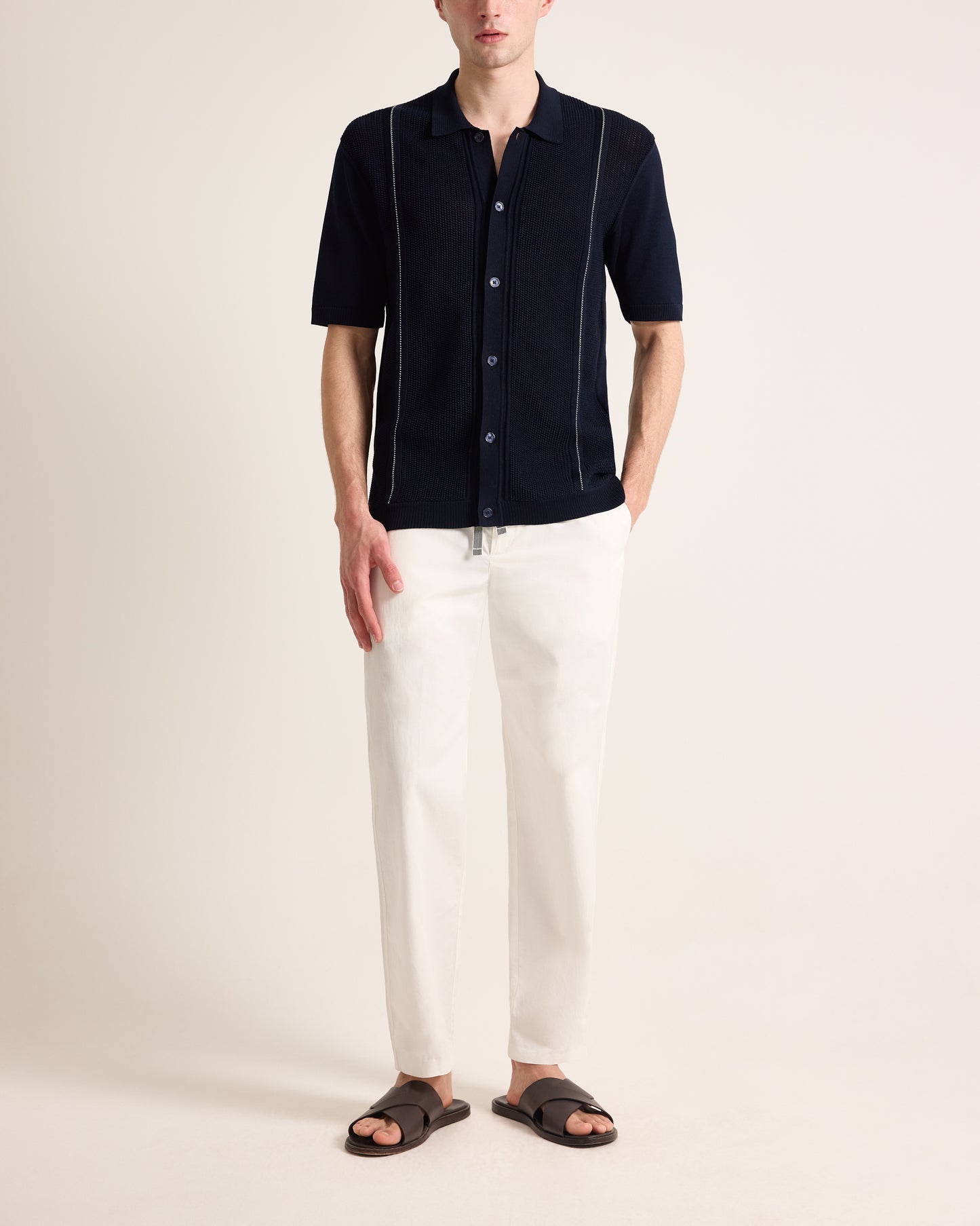 Man wearing a dark blue shirt with white pants on a plain background