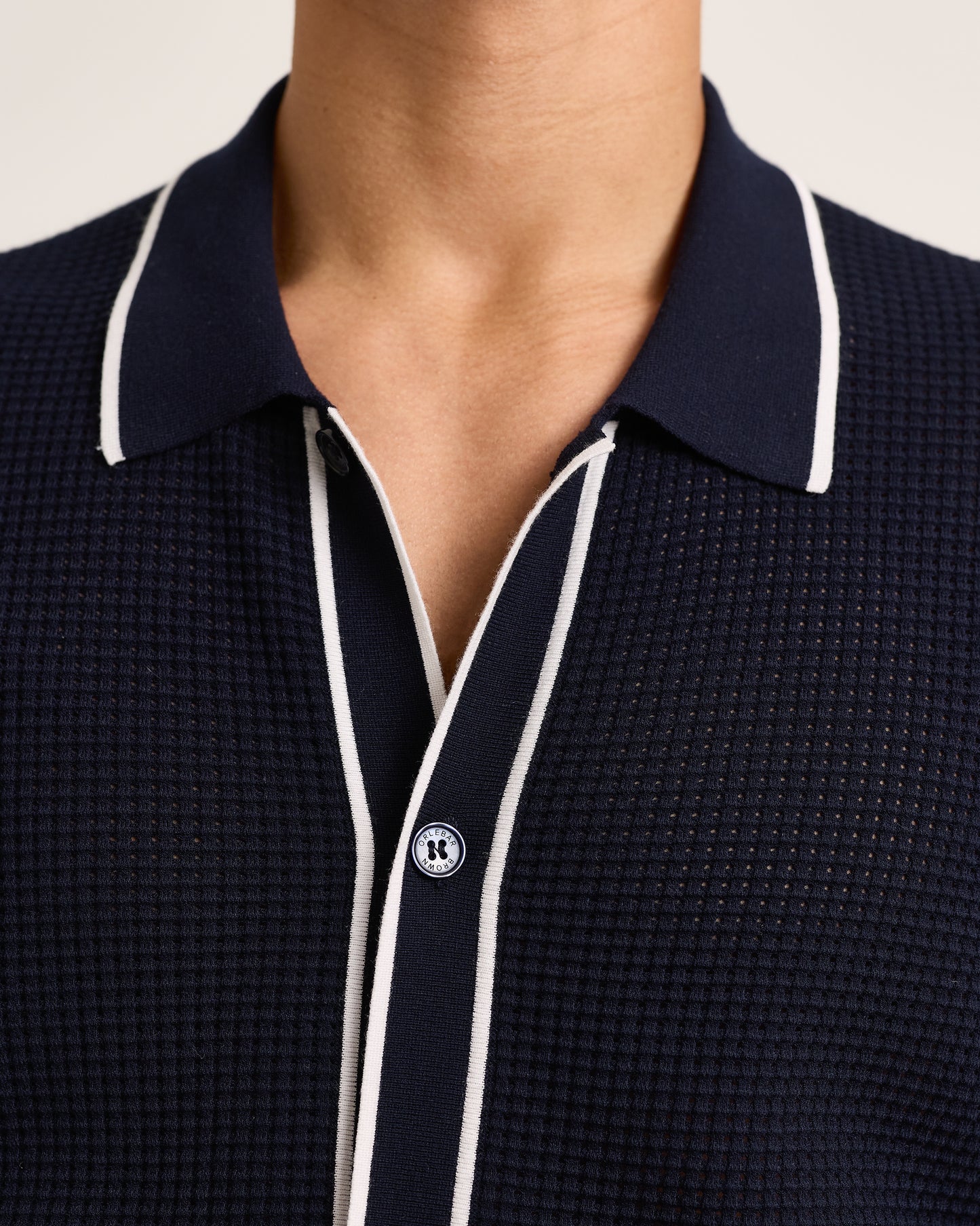 Closeup of navy knitted shirt with white trim on a plain background