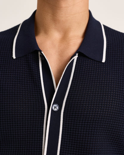 Closeup of navy knitted shirt with white trim on a plain background