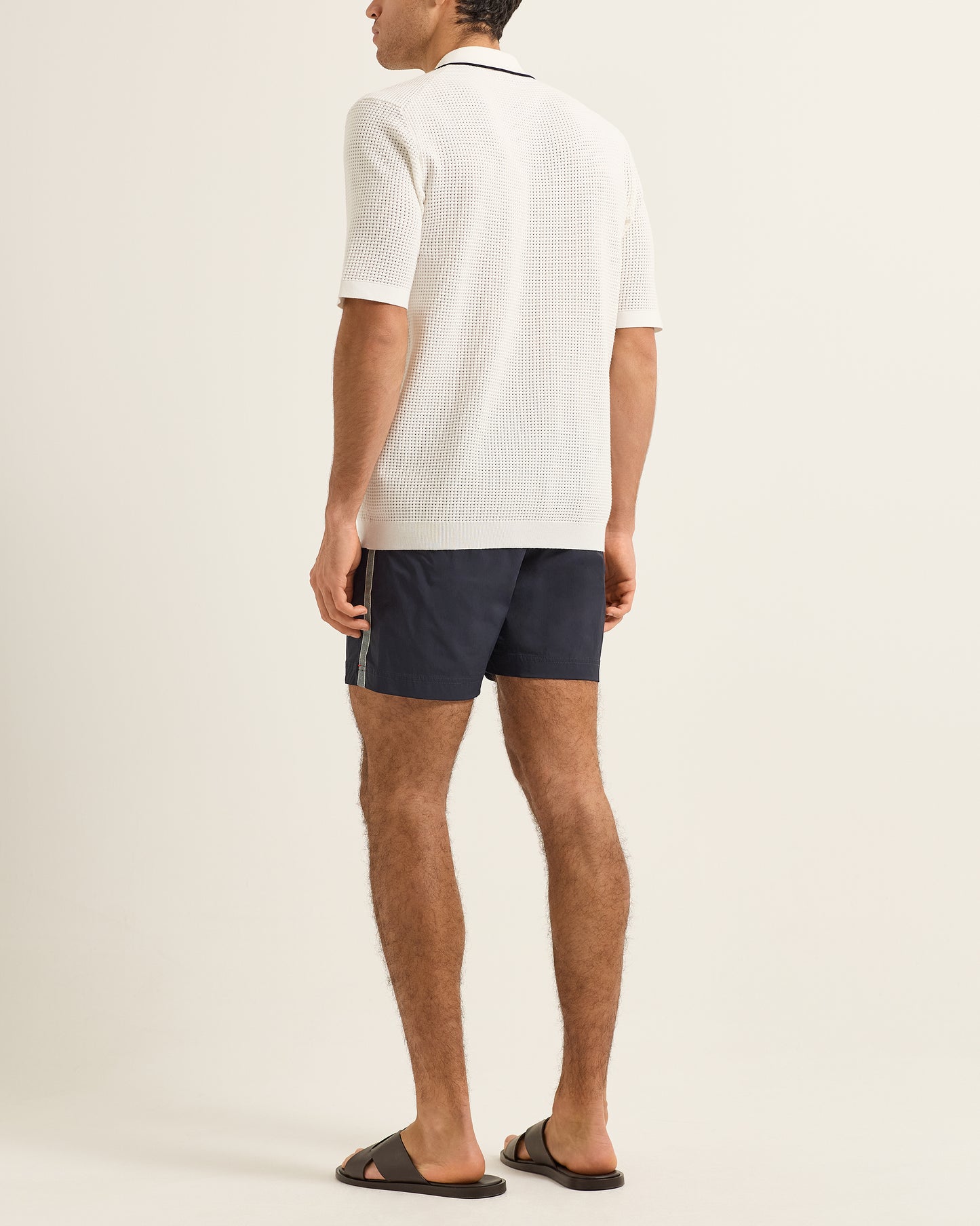 Man wearing a white polo shirt and navy shorts on a plain background