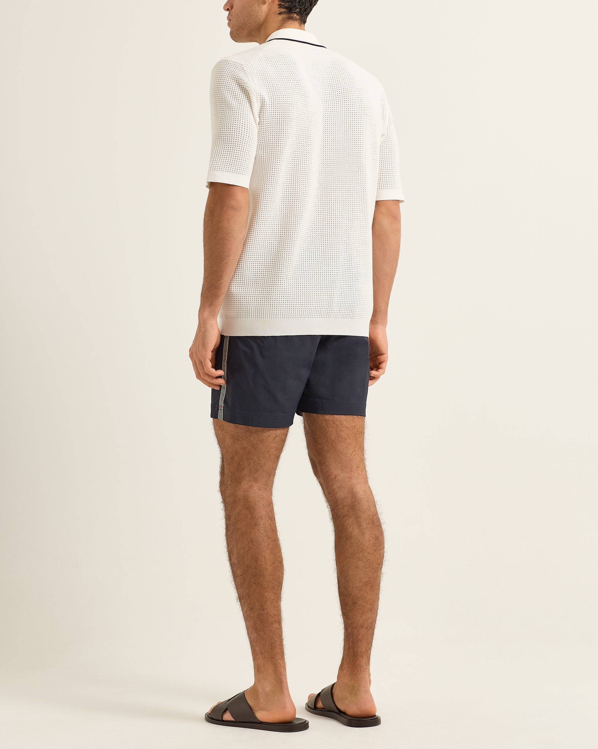 Man wearing a white polo shirt and navy shorts on a plain background