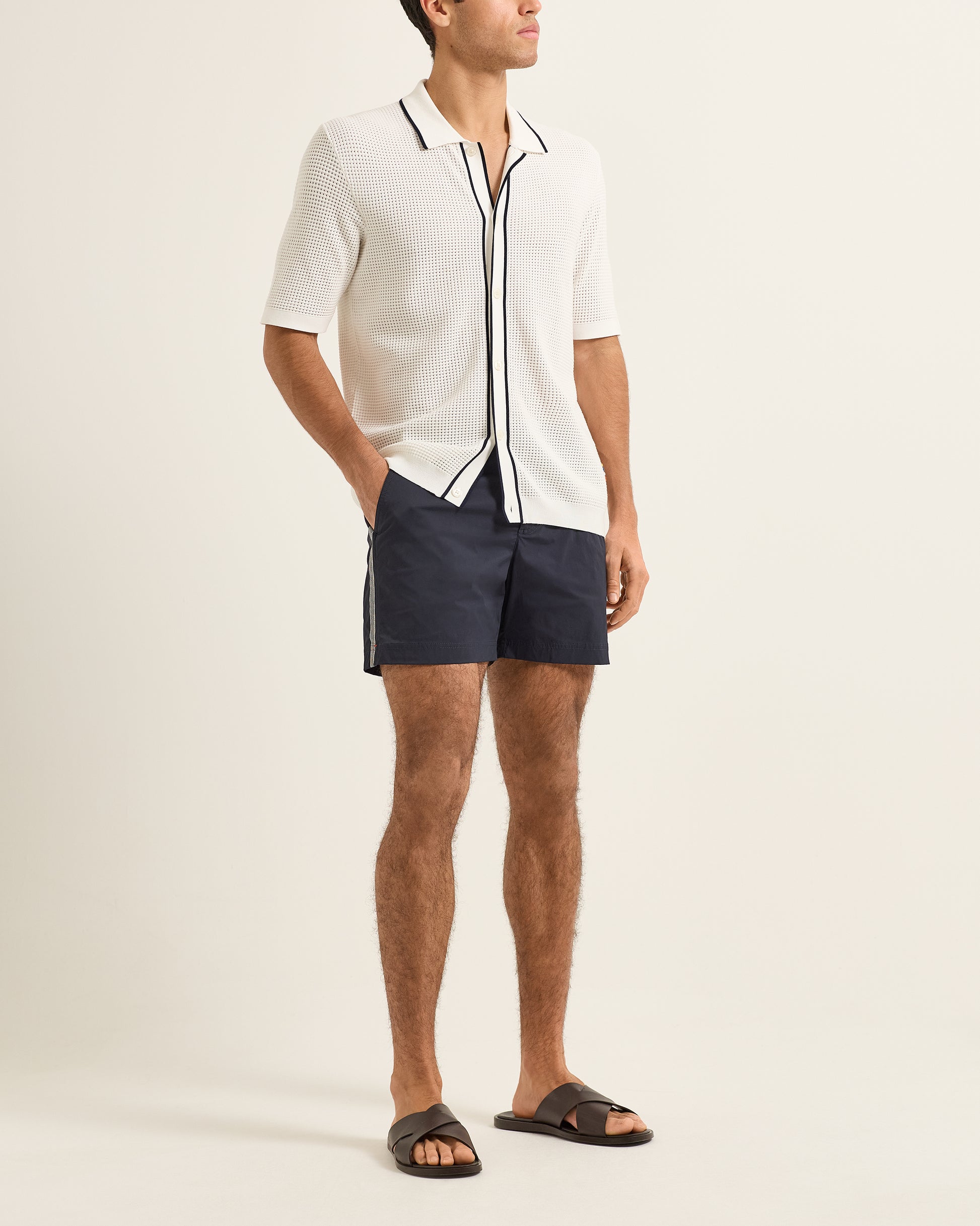 Person wearing a white polo shirt with black trim and dark shorts on a plain background