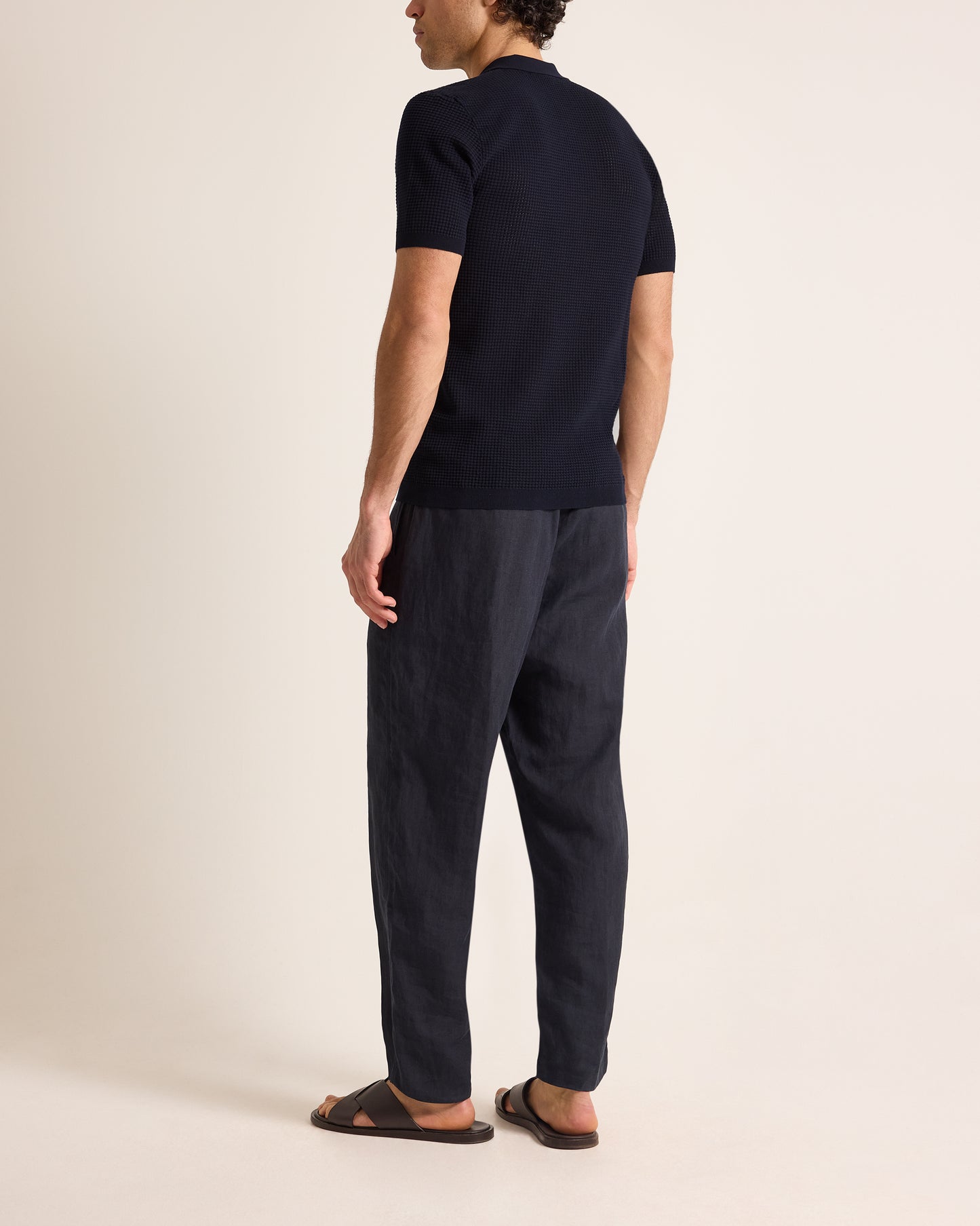 Man wearing a navy polo t-shirt and dark pants on a beige background